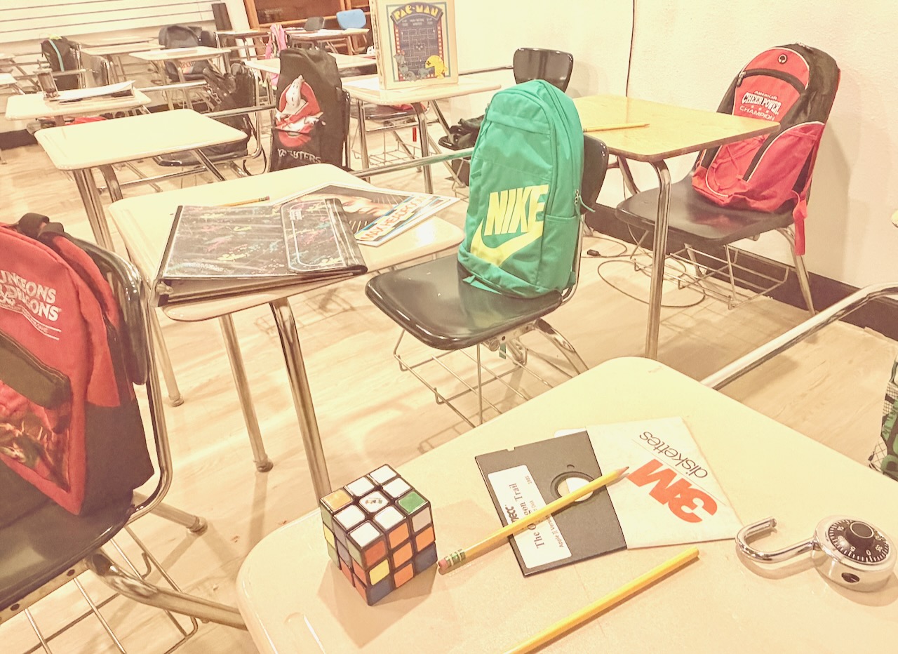 Classroom with desks, chairs, backpacks, a Rubik's cube, and stationery on tables.