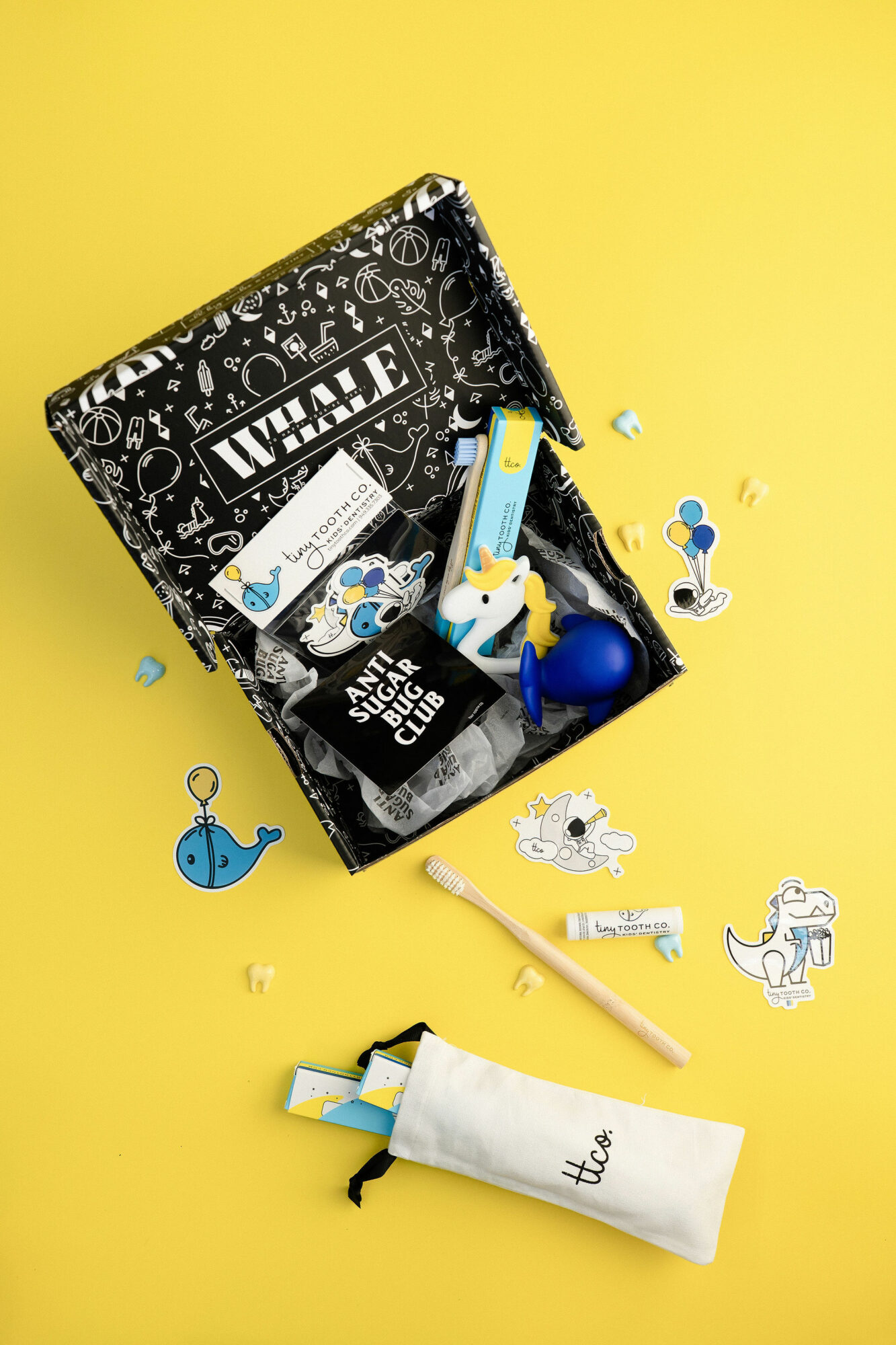 Open box with art supplies and toys spilling onto yellow surface, including a paintbrush, whale, and robot figure.