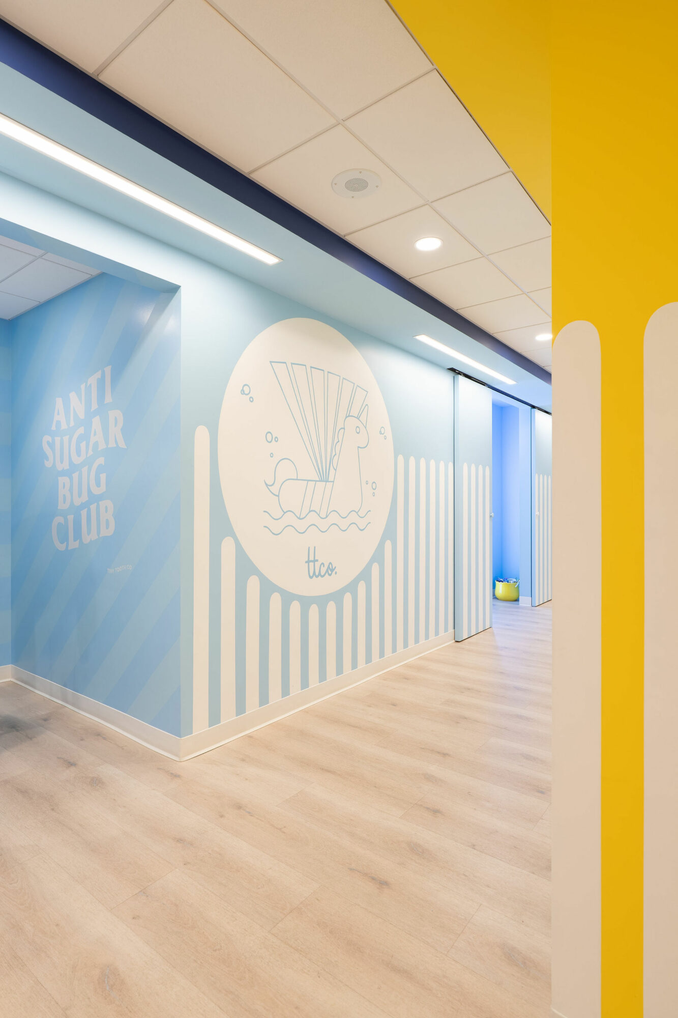 Interior wall with blue and white design, logo, and text reading 'Anti Sugar Bug Club', with wooden flooring.
