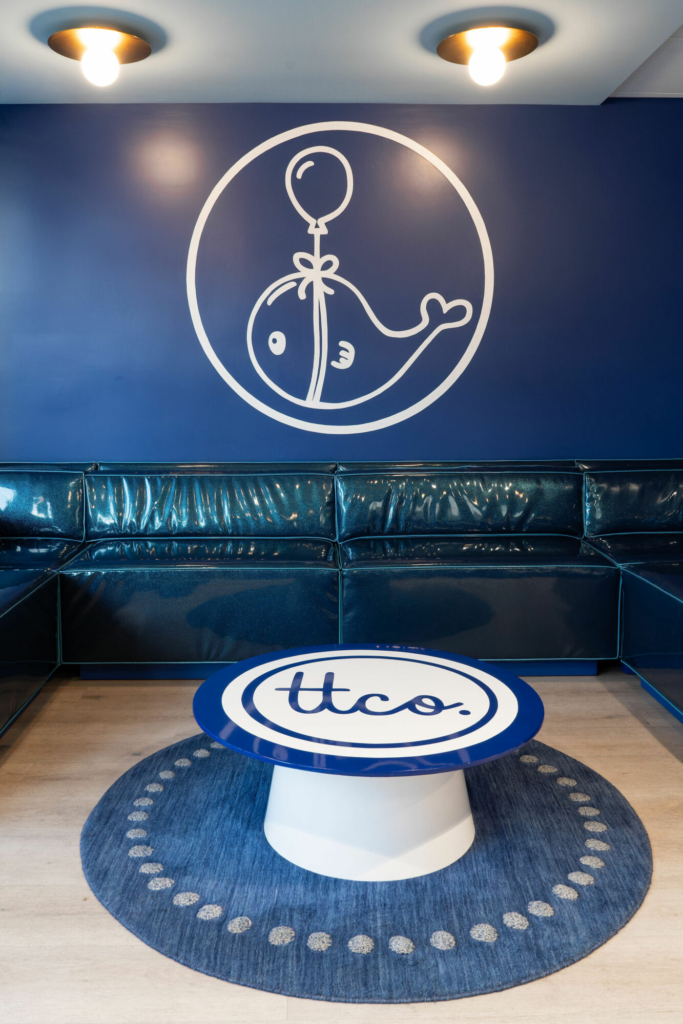 Wall art of a balloon and whale inside a circle, above a blue sofa, with a round table and rug in front.