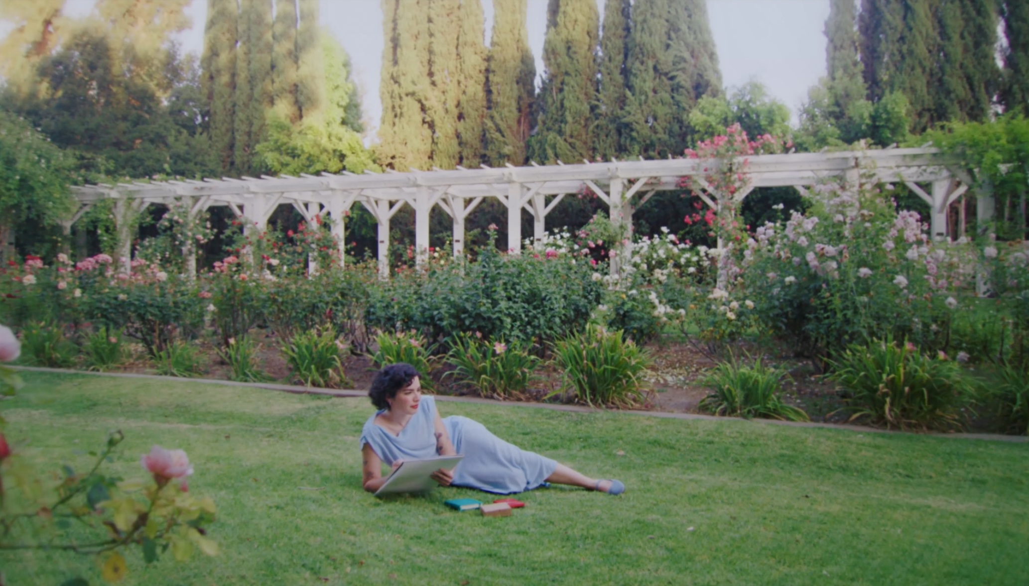 Person lying on grass in a garden with flowers and trees in the background.