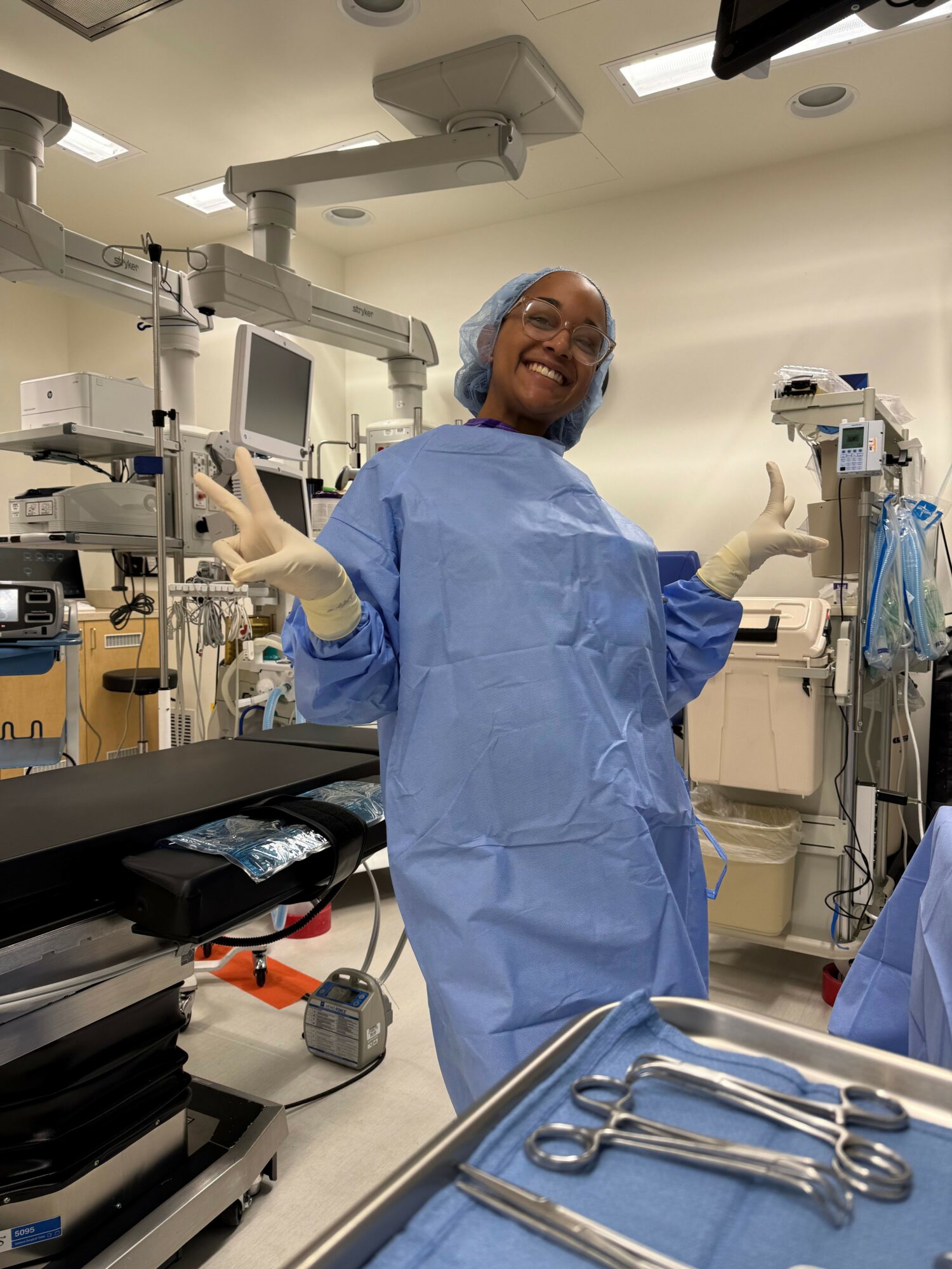 Medical professional in blue gown and gloves standing in operating room with surgical instruments on table.