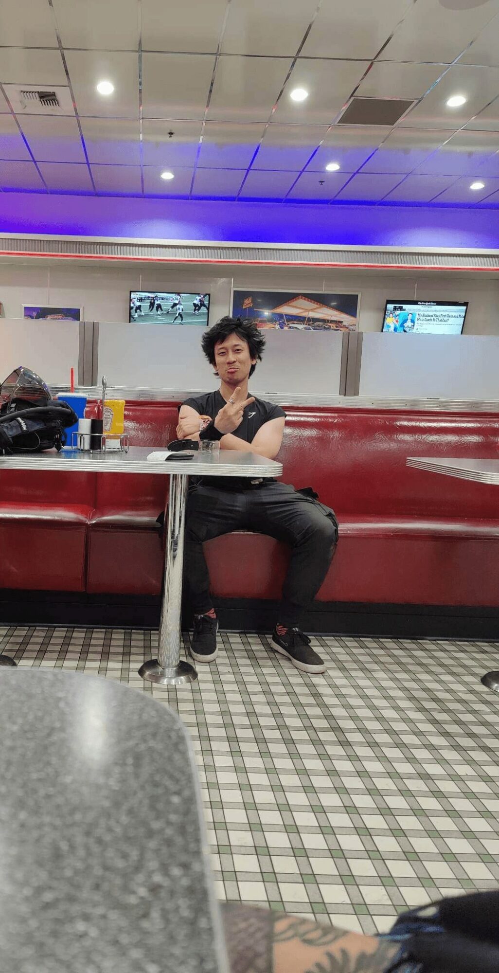 Person sitting on a red booth seat in a public space, with a table and screens on the wall behind.
