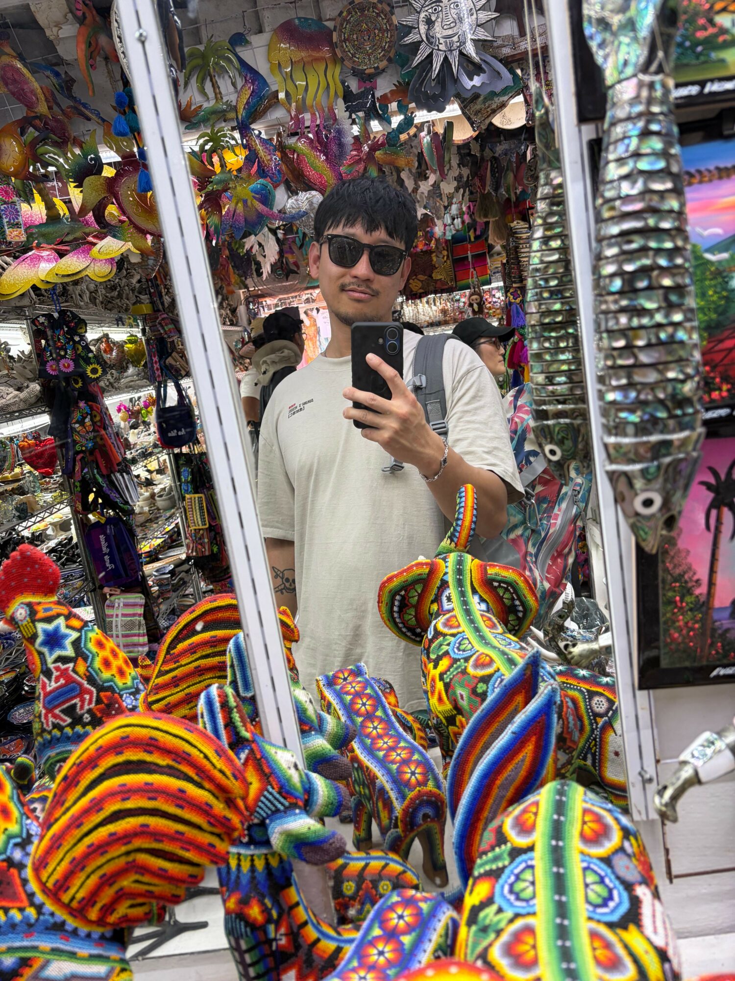 Person wearing colorful, patterned clothing and a hat, browsing items at a market stall with various colorful goods.