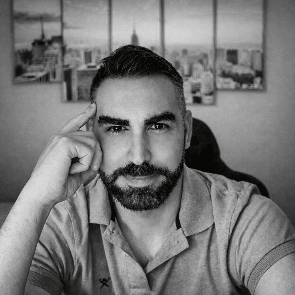 Man with beard and short hair, resting his head on his hand, in front of cityscape artwork, in black and white.
