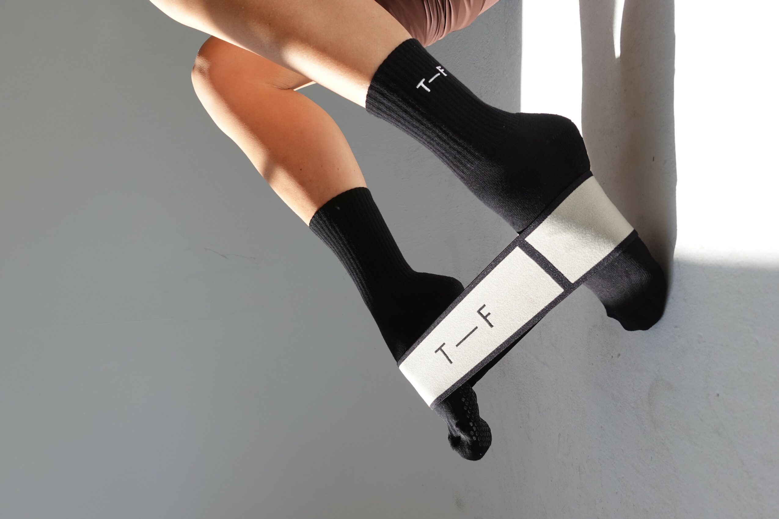 Person wearing black socks and platform shoes, sitting on a windowsill with natural light, legs crossed.