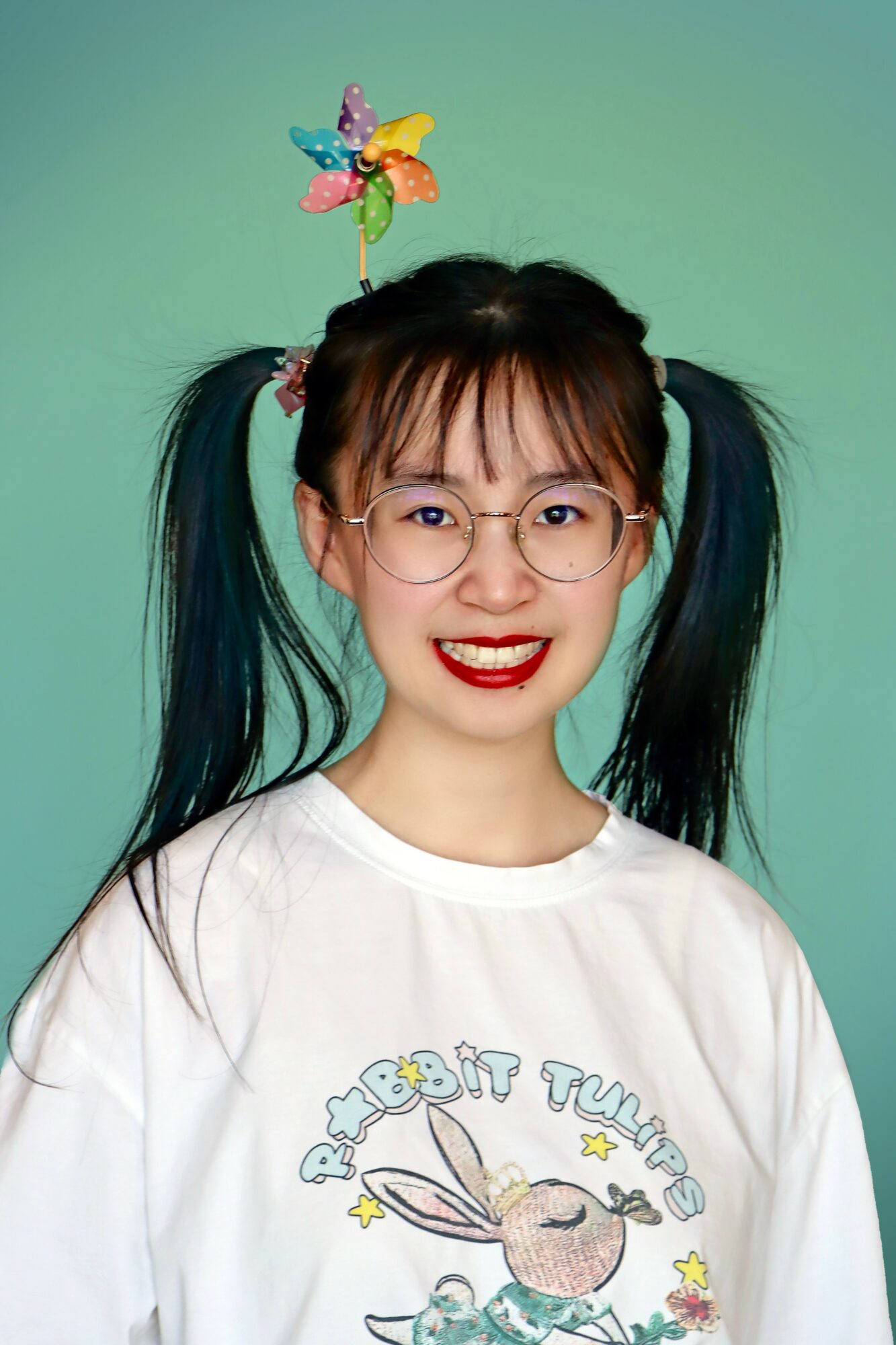 Young woman with glasses and pigtails, smiling, wearing a white T-shirt with a bunny and star design, against a green background.