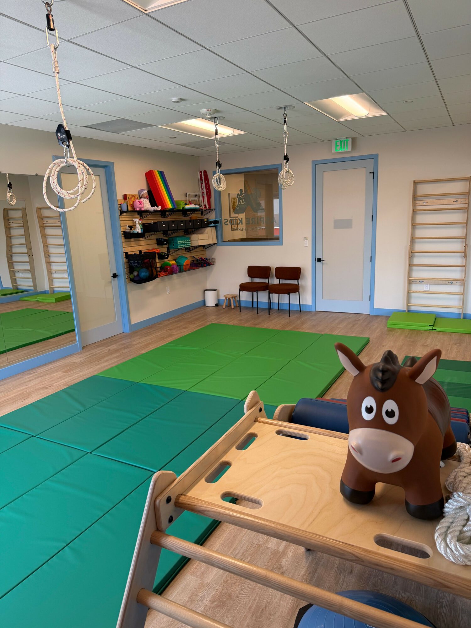 Children's playroom with a large brown cow toy, green and blue foam mats, and a wooden table with chairs.