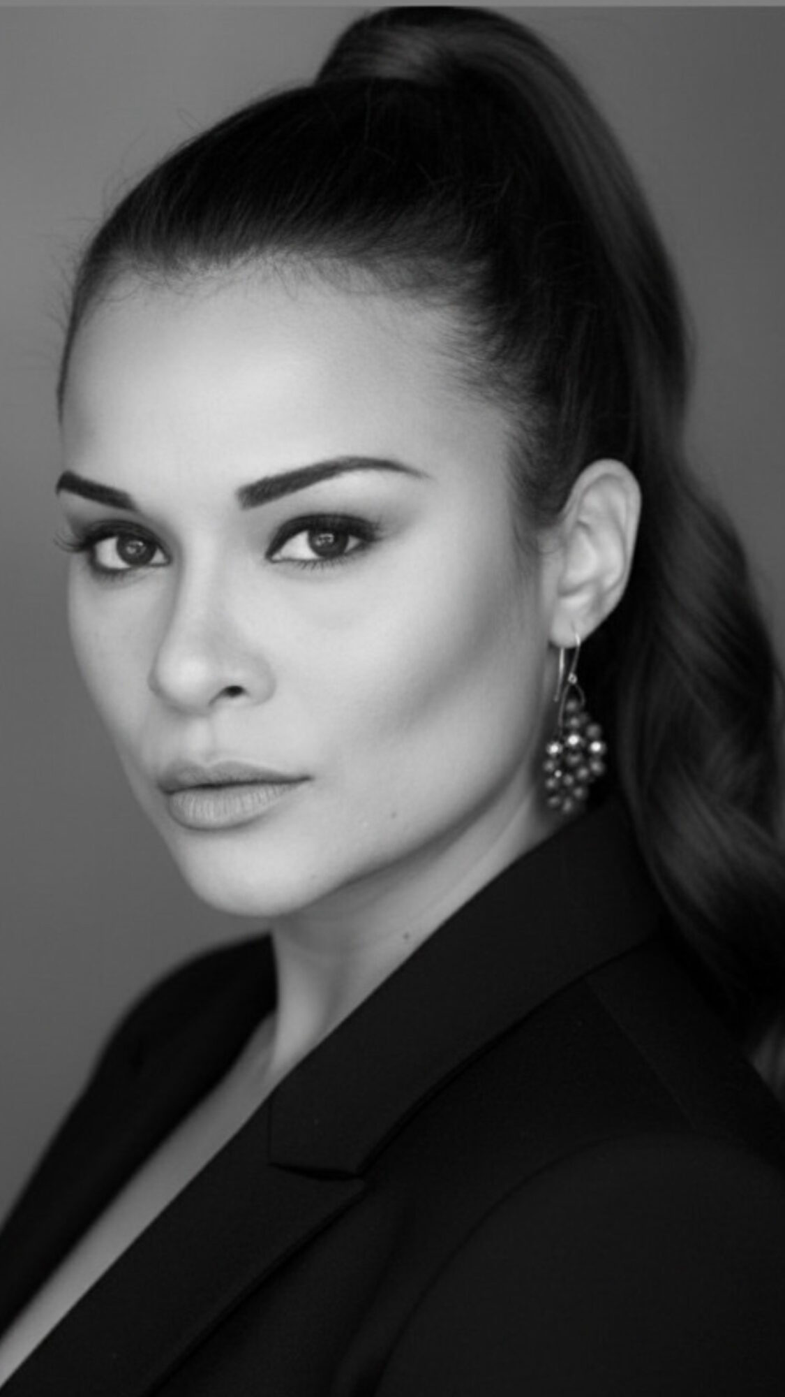 Portrait of a woman with high ponytail, earrings, and confident expression, in black and white.