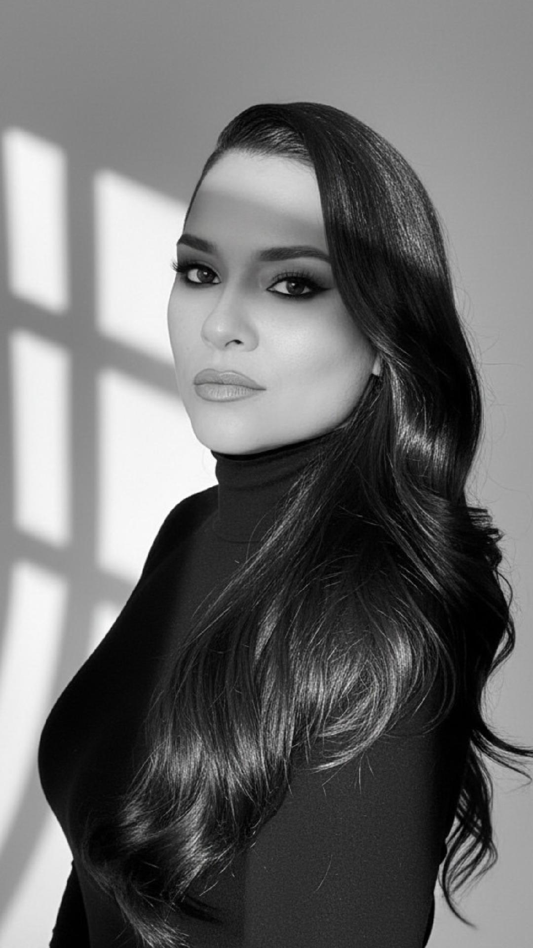 Portrait of a woman with long, wavy hair and makeup, wearing a turtleneck, in black and white.