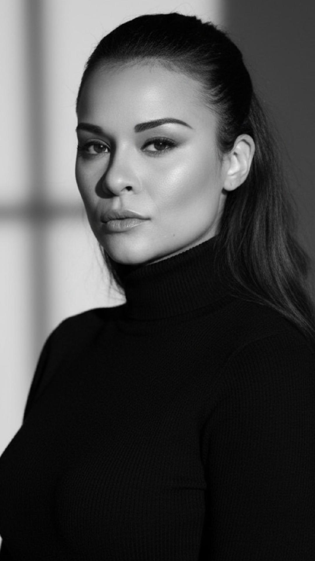 Black and white portrait of a woman with long hair, wearing a turtleneck, looking at the camera with a serious expression.