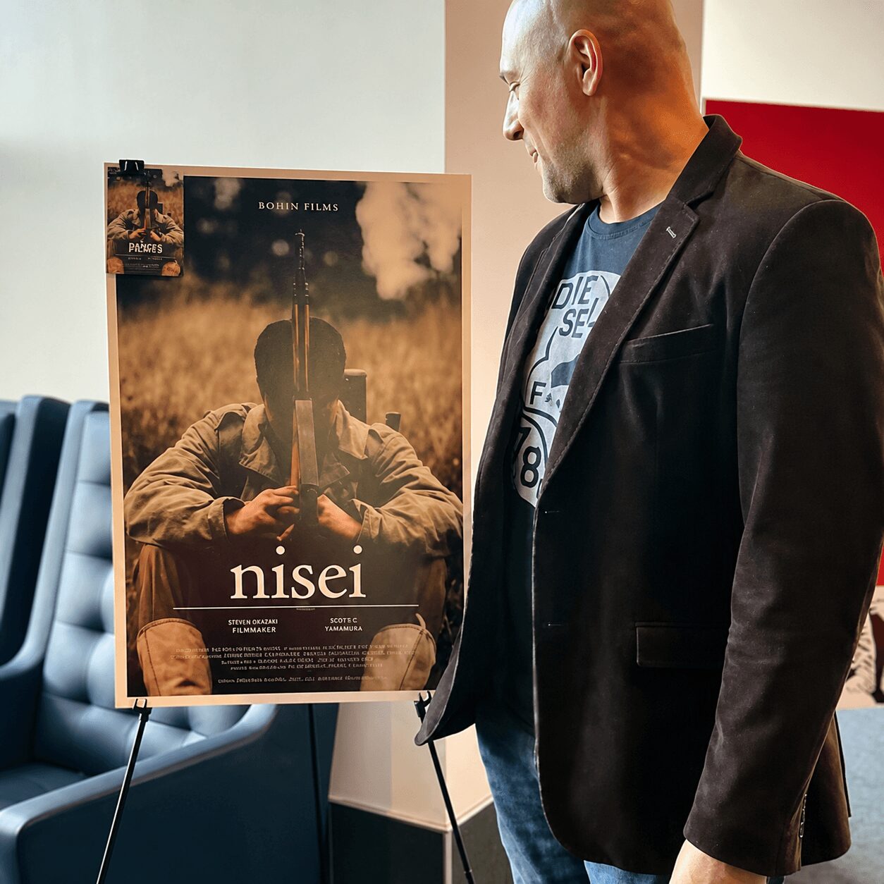 Man in black blazer looking at a movie poster with a person holding a violin case, titled 'nisei'.