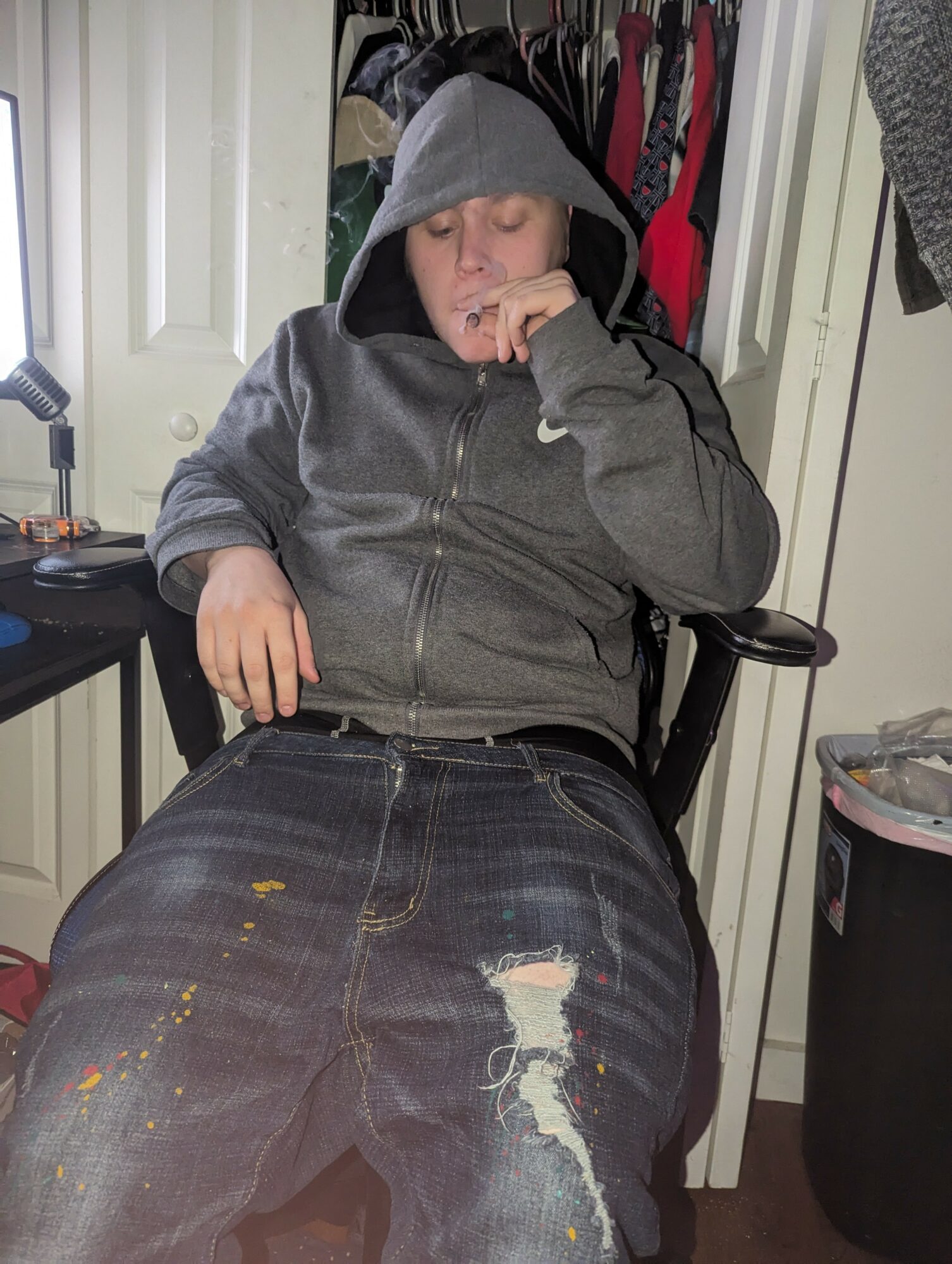 Person sitting in a chair wearing a gray hoodie and ripped jeans, with a closet and door in the background.