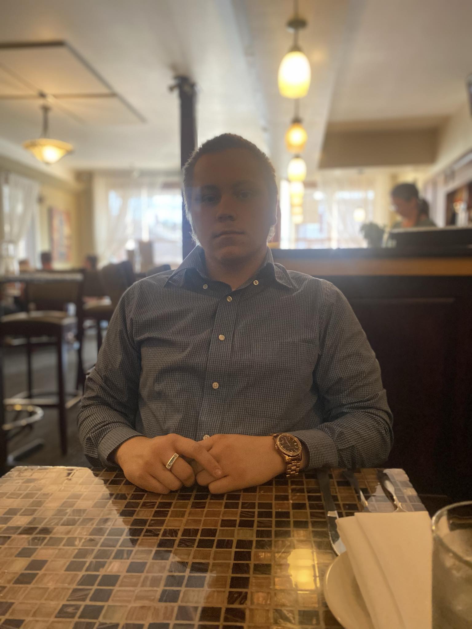 Young man sitting at a table in a restaurant, with warm lighting and background patrons.