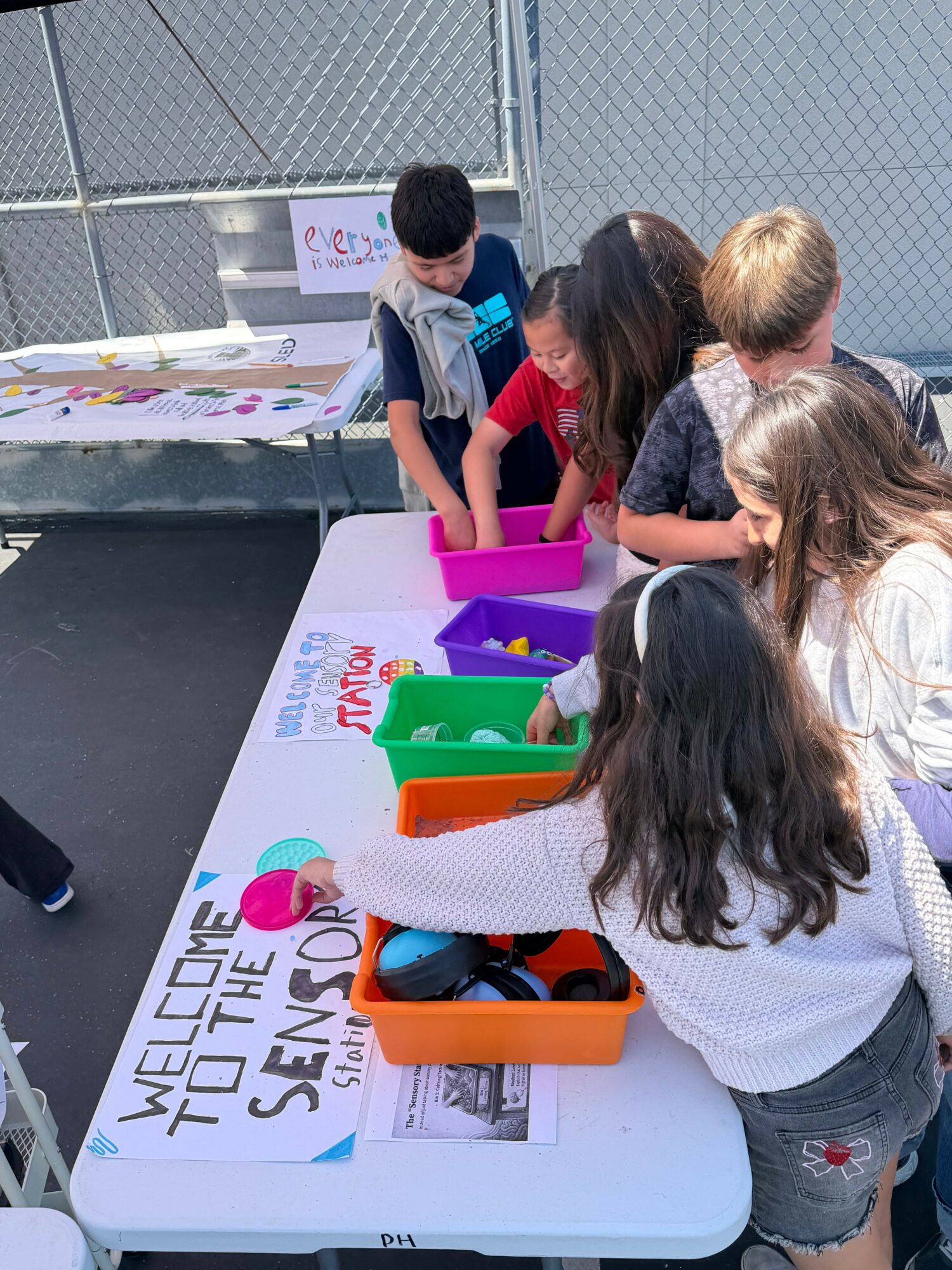 Group of children gathered around a table with colorful boxes, engaging in an activity outdoors.