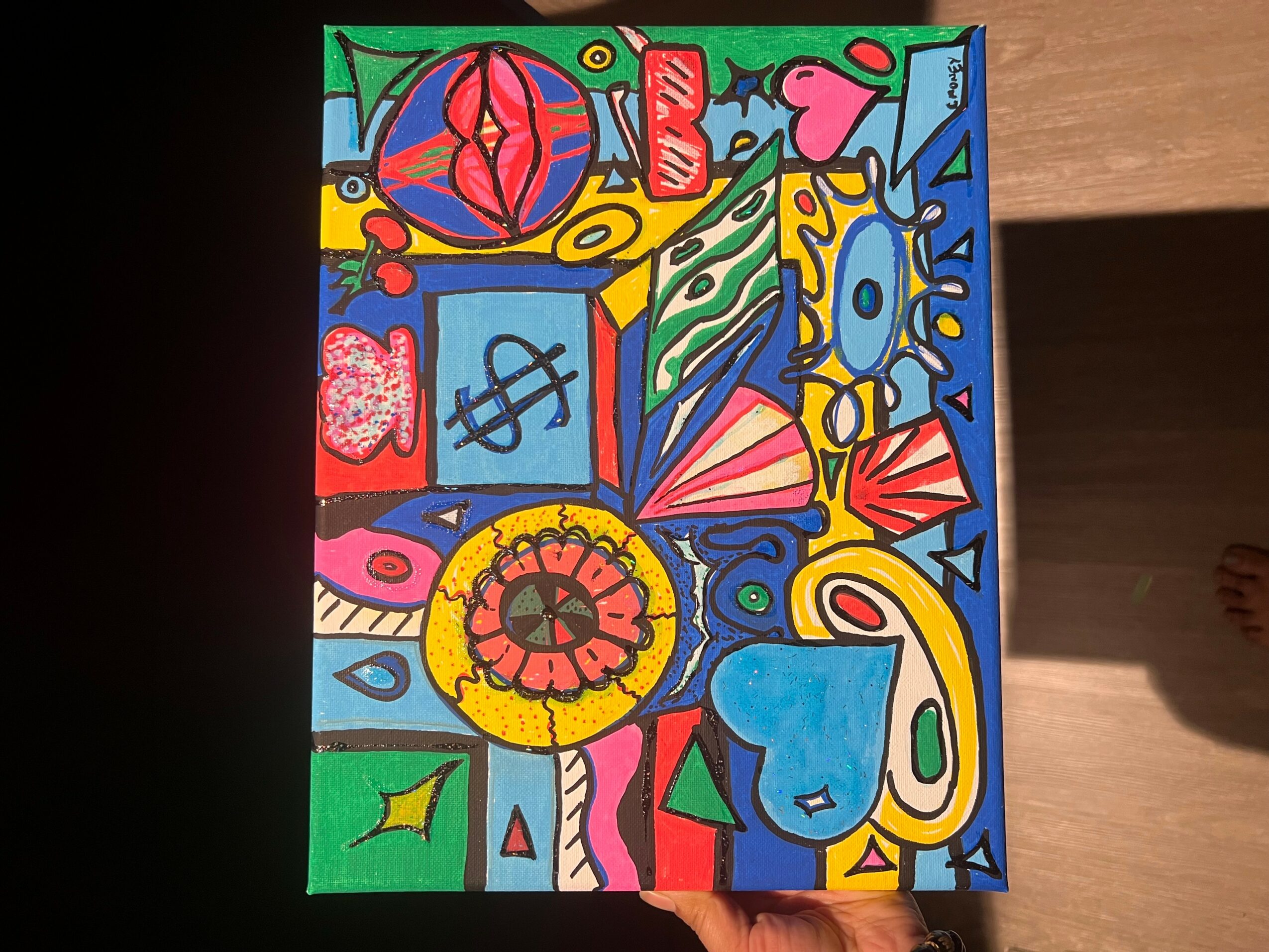 Colorful abstract drawing with shapes, patterns, and symbols on a rectangular surface, placed on a wooden background.