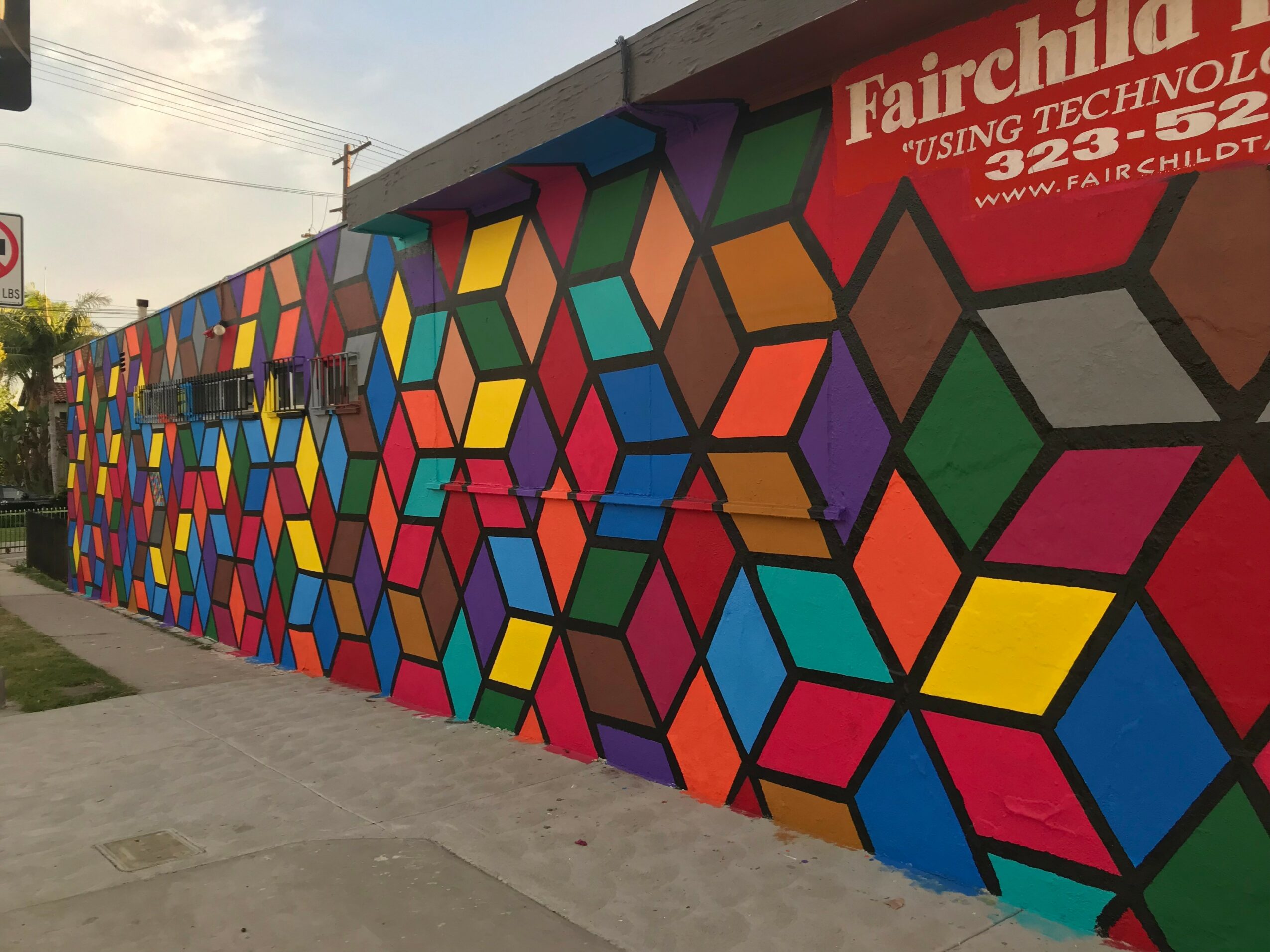 Colorful geometric mural on a wall with a sign for Fairchild using technology, featuring various shapes and bright colors.