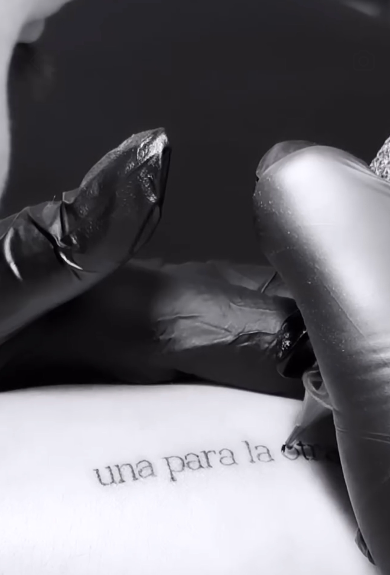 Close-up of hands wearing black gloves holding a silver object, with partially visible text in Spanish.