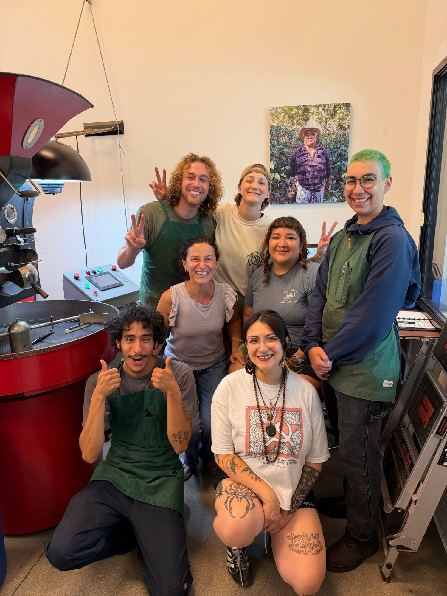 Group of six people in a room with artwork on the wall, some making peace signs, standing around a red table.