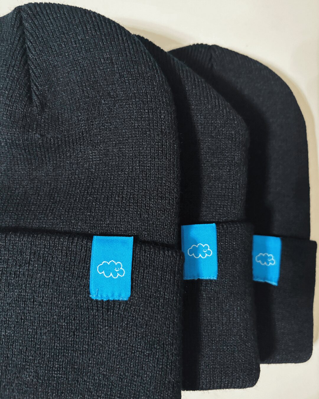 Three black backpacks with blue tags featuring cloud icons, stacked together against a light background.