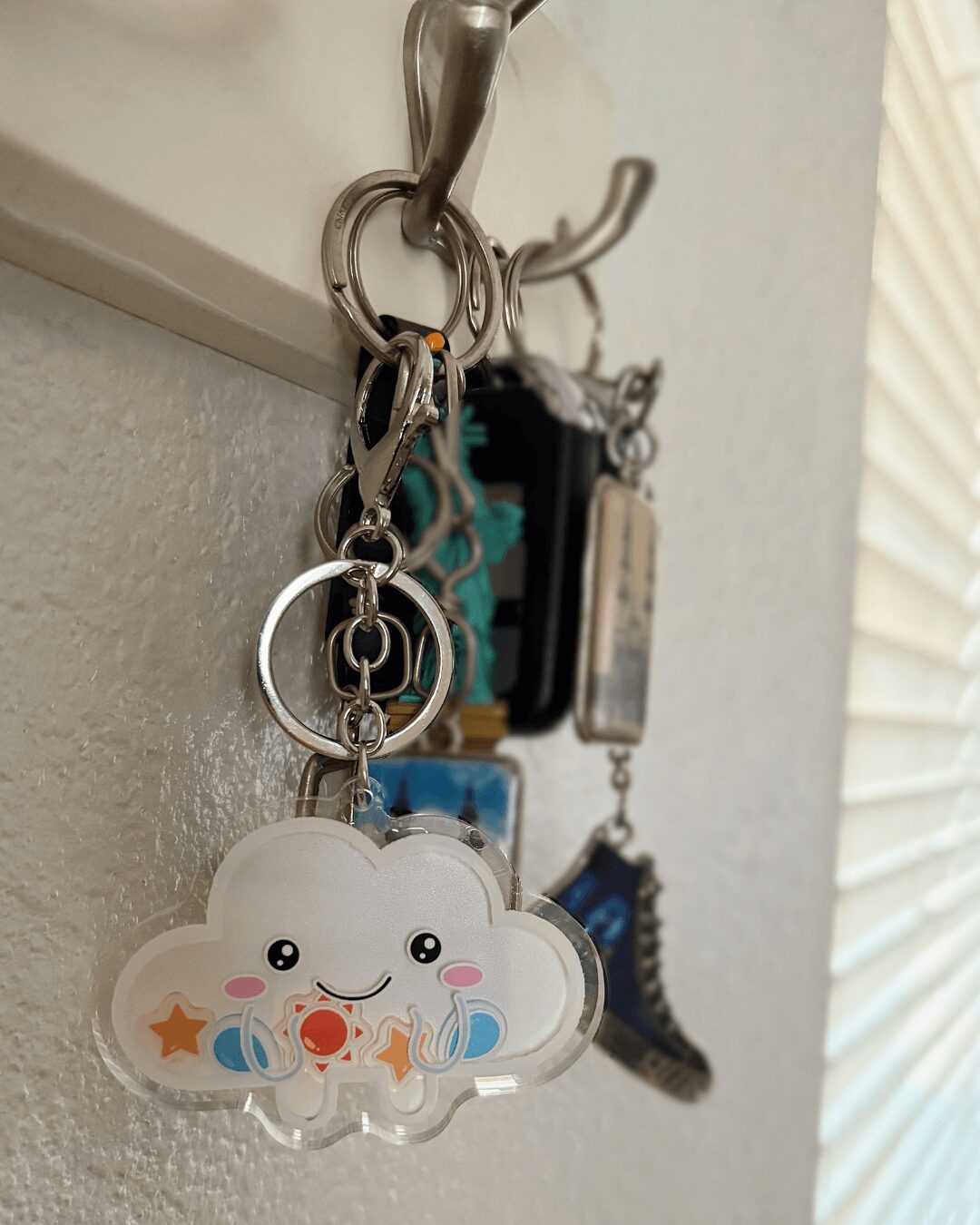 Keychain with a smiling cloud, stars, and raindrops hanging from a hook, with other keychains in the background.