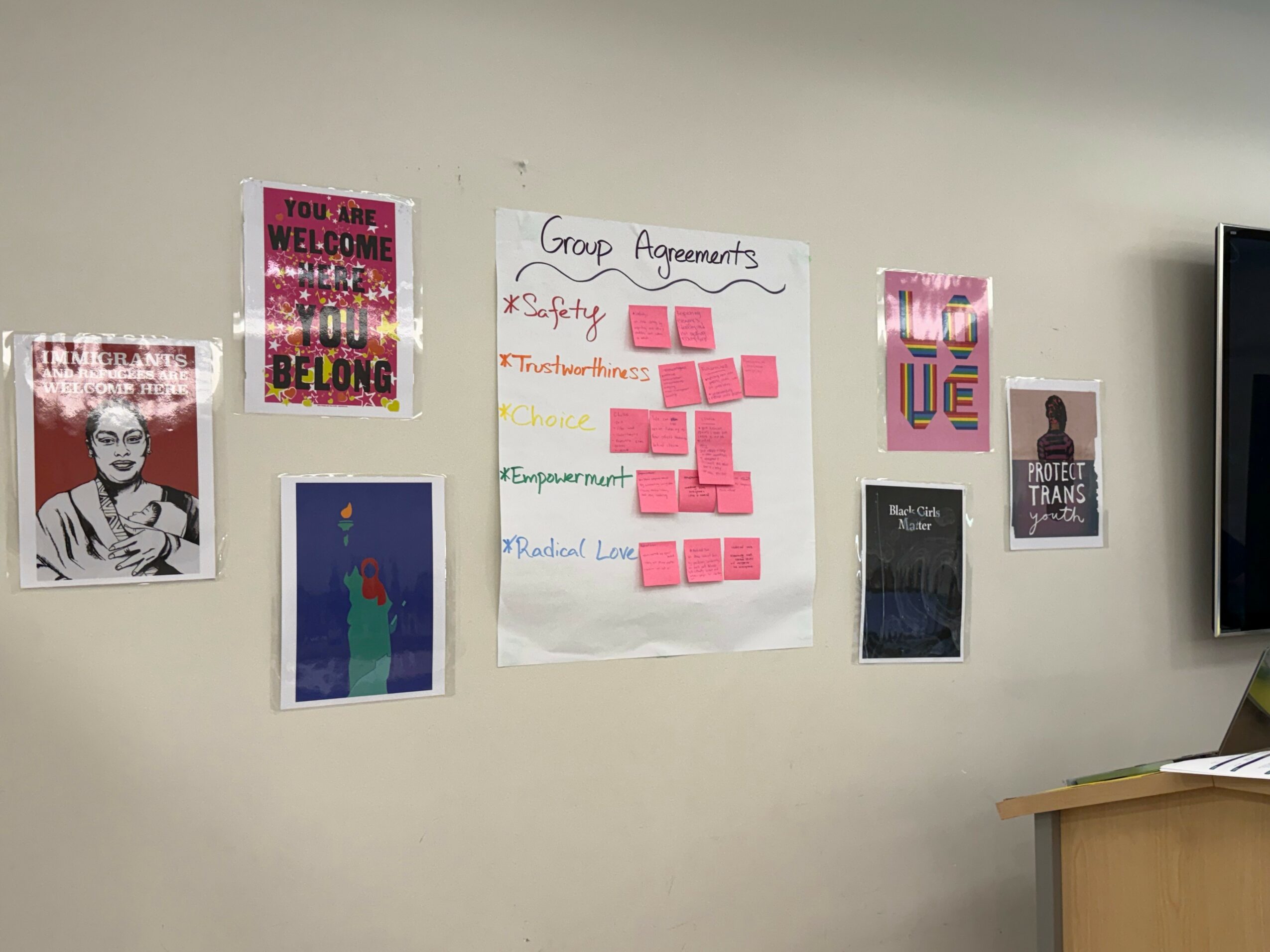 Wall with posters, sticky notes, and a large paper titled 'Group Agreements' in a room.