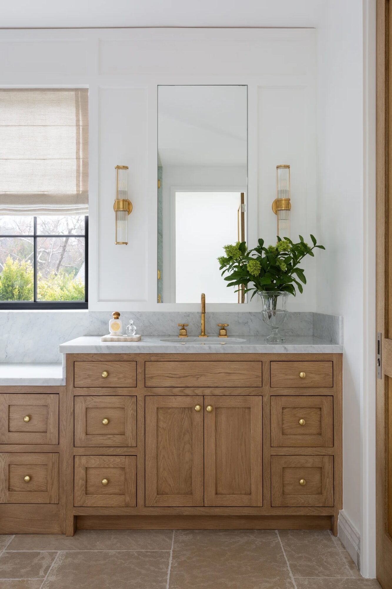 Bathroom vanity with wooden cabinets, marble countertop, large mirror, potted plant, and window with a blind.