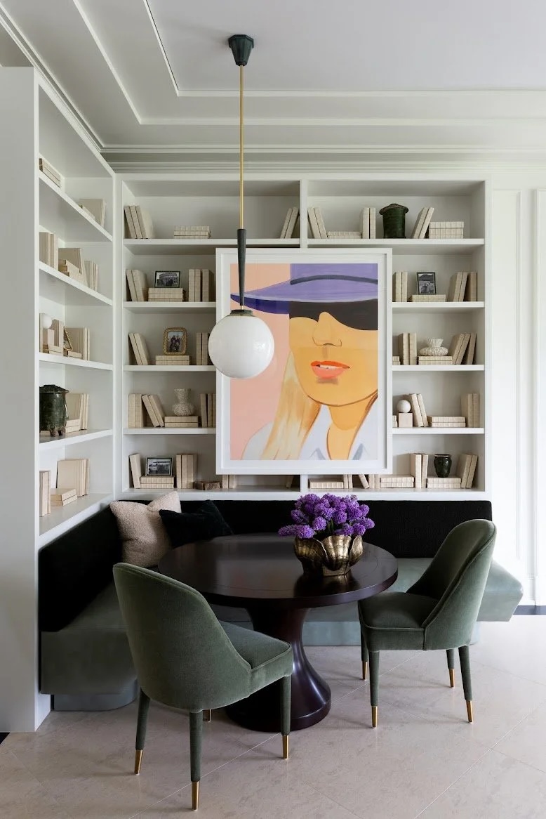 Living room with a large framed portrait of a woman wearing sunglasses, bookshelves, a round table with purple flowers, and four chairs.