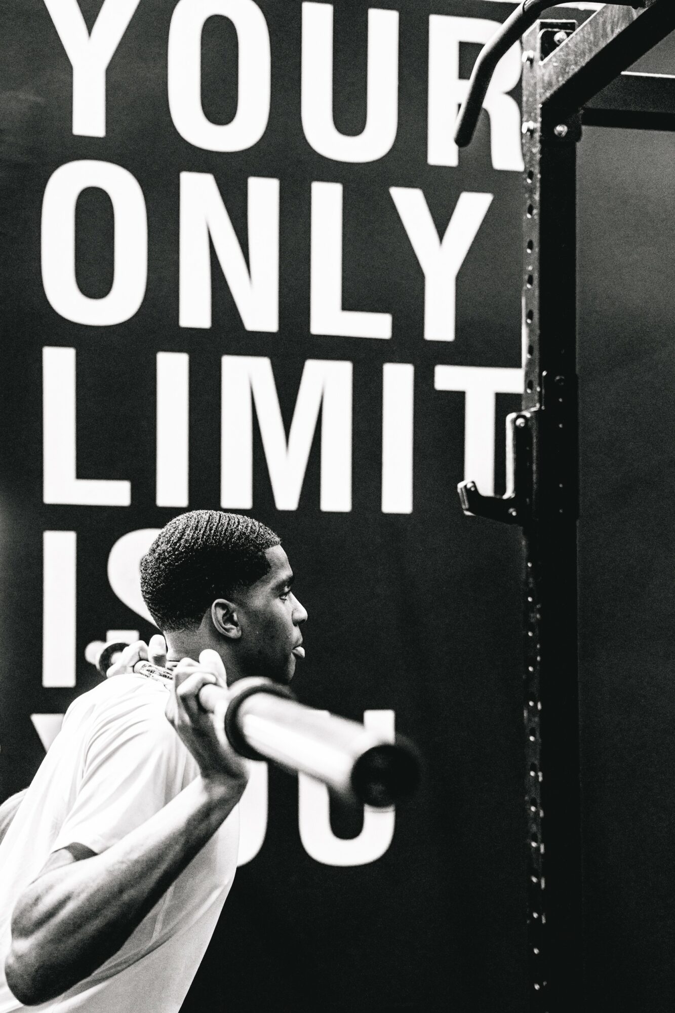 Young man holding a barbell in a gym, with a large sign reading 'YOUR ONLY LIMIT' in the background.