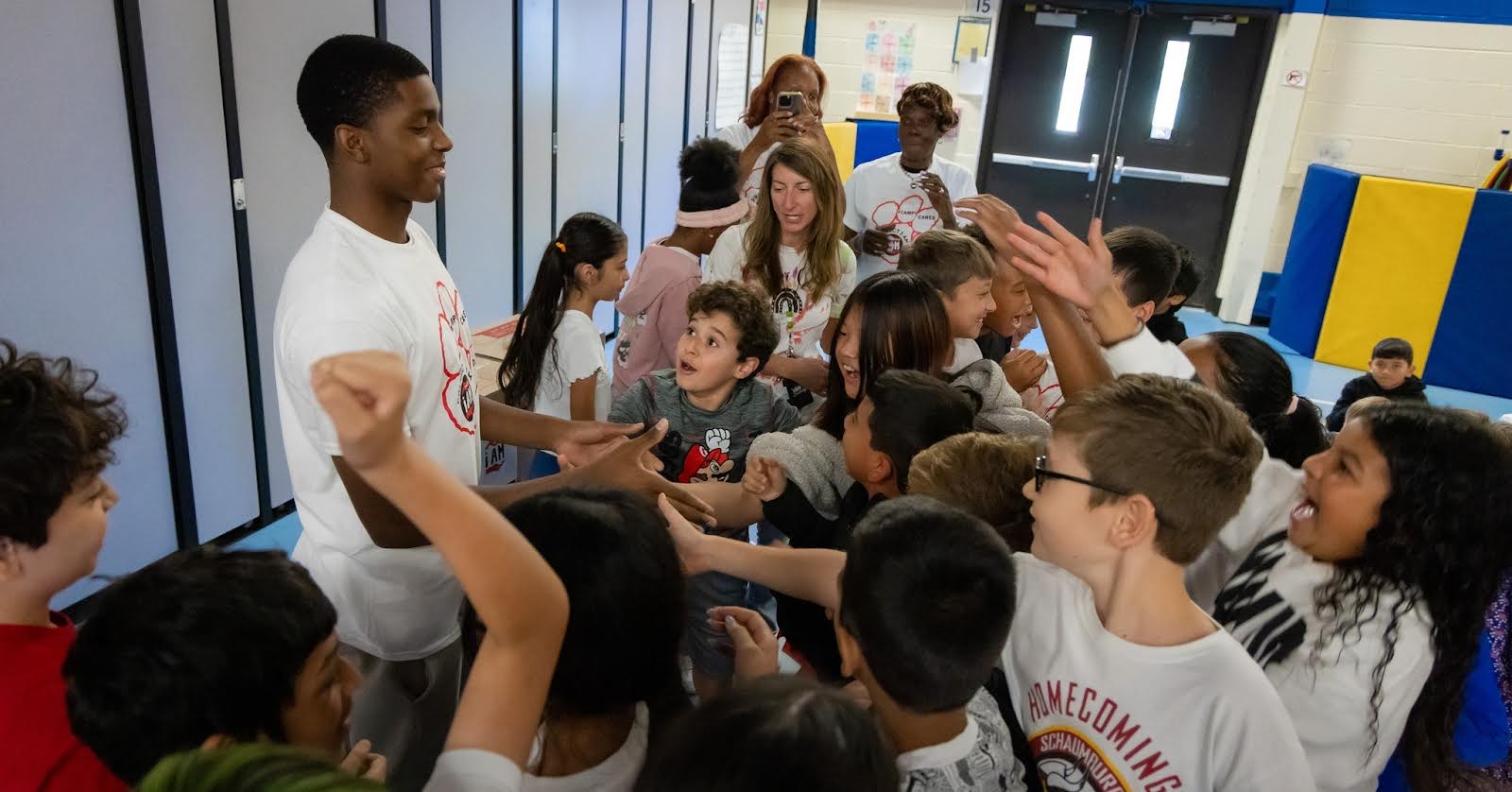 Group of children and a young adult in a school hallway, engaging in conversation and activities.