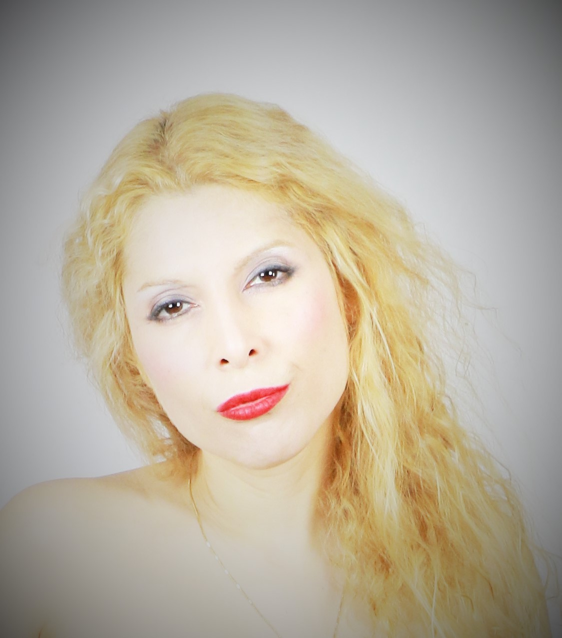 Portrait of a woman with long, wavy blonde hair, light makeup, and red lipstick, looking at the camera.
