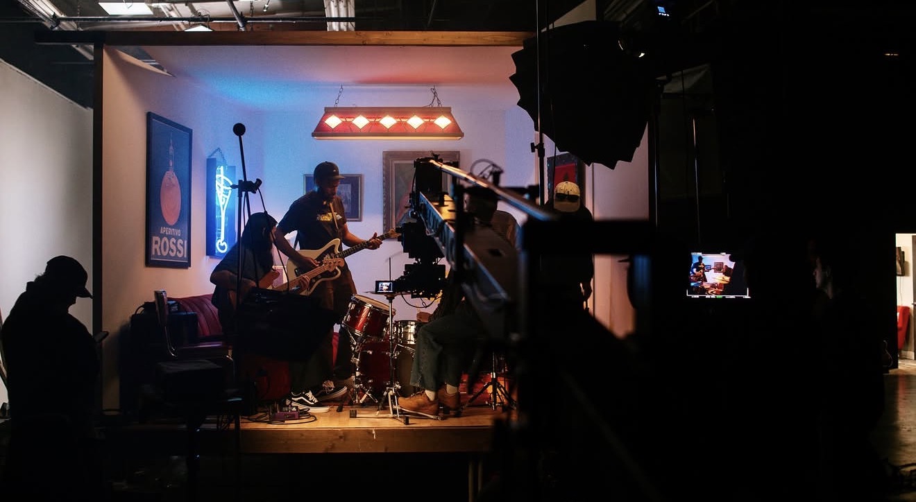 Band performing on stage with instruments, audience watching in a dimly lit venue.