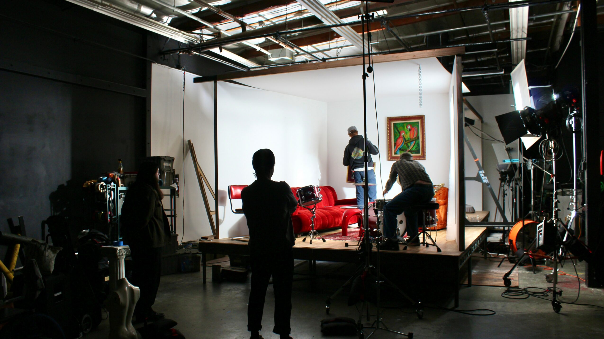 A film or photo studio with a white backdrop, red sofa, and people setting up equipment and lighting.