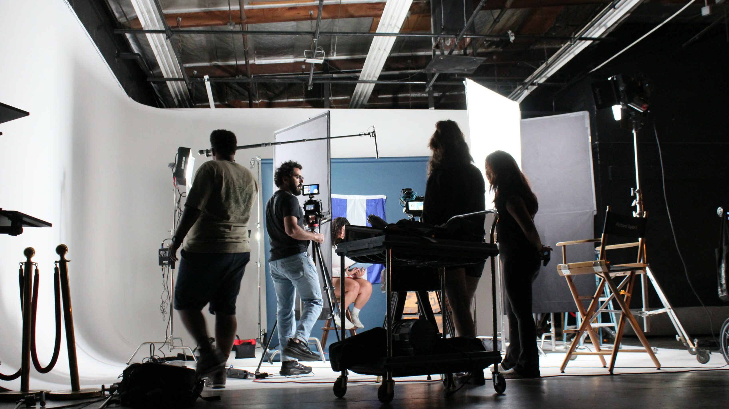 People working in a studio with lighting and equipment, some using computers and others standing around a keyboard.