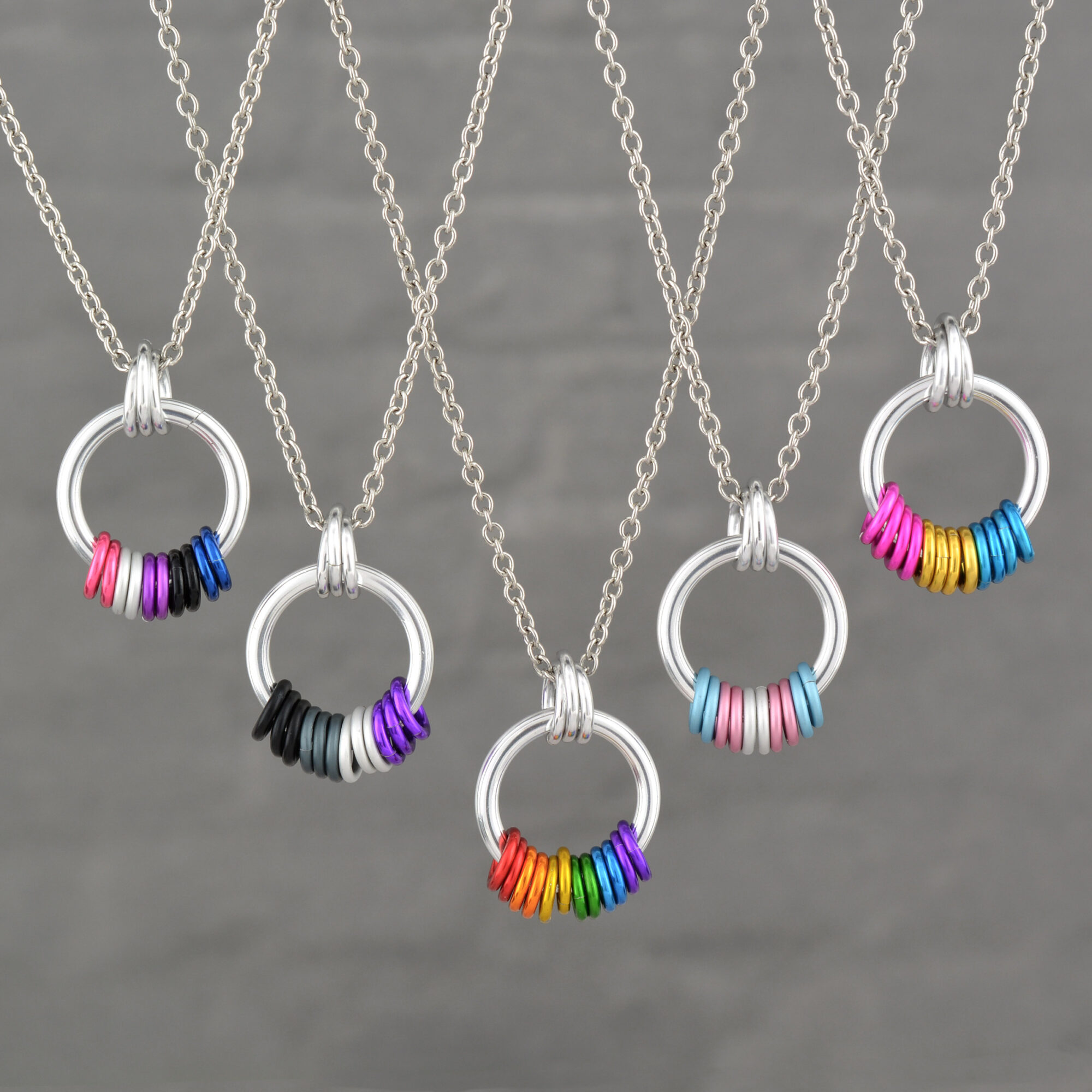 Four necklaces with circular pendants and colorful beads, displayed against a gray background.