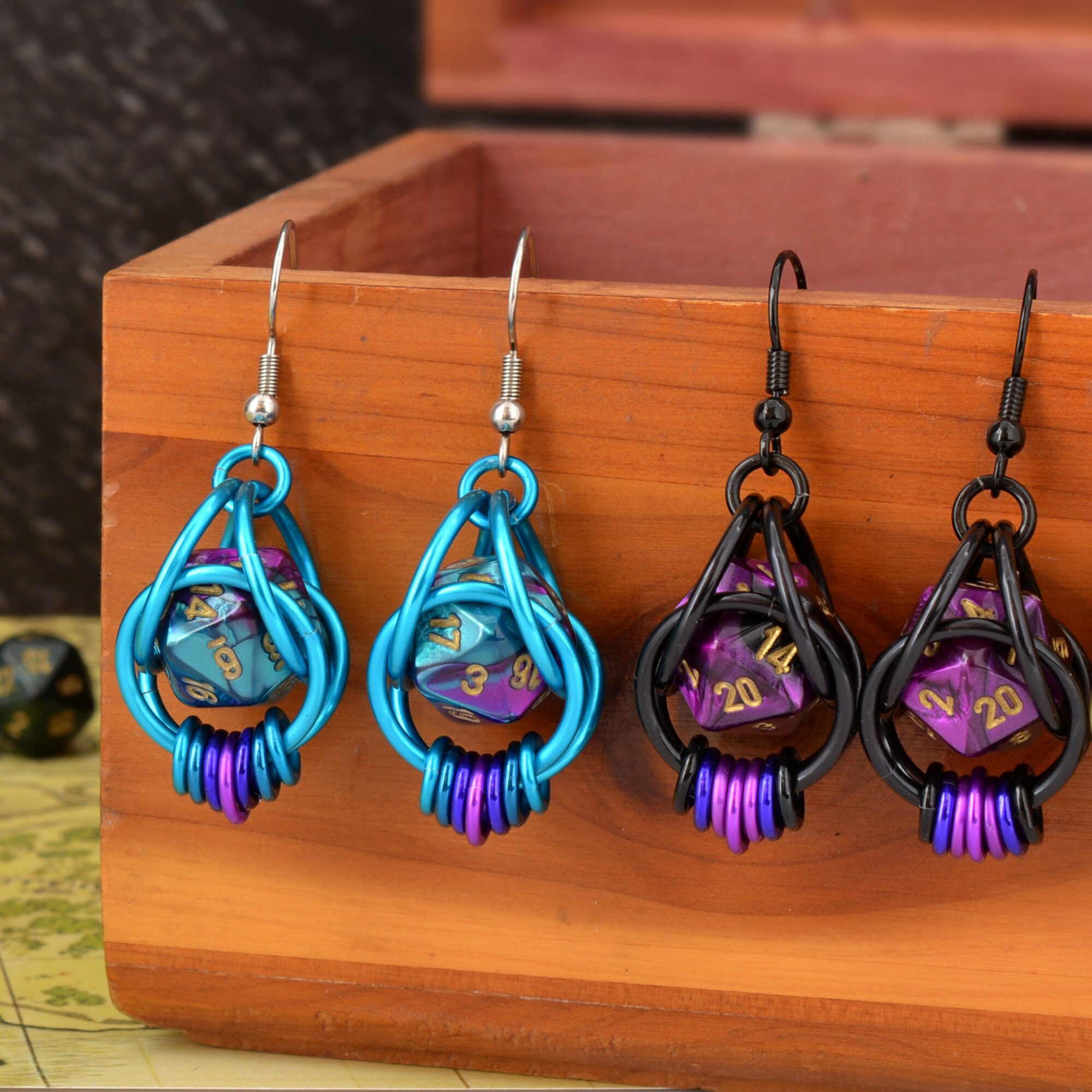 Two pairs of colorful earrings with purple beads, displayed on a wooden surface, one pair in blue and the other in black.