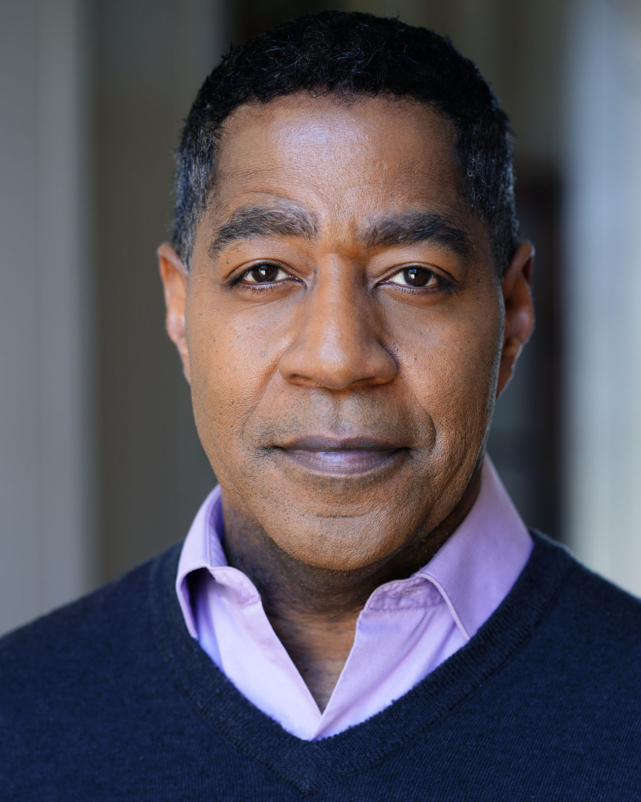Portrait of a man with short dark hair, wearing a purple collared shirt and dark sweater, looking at the camera.