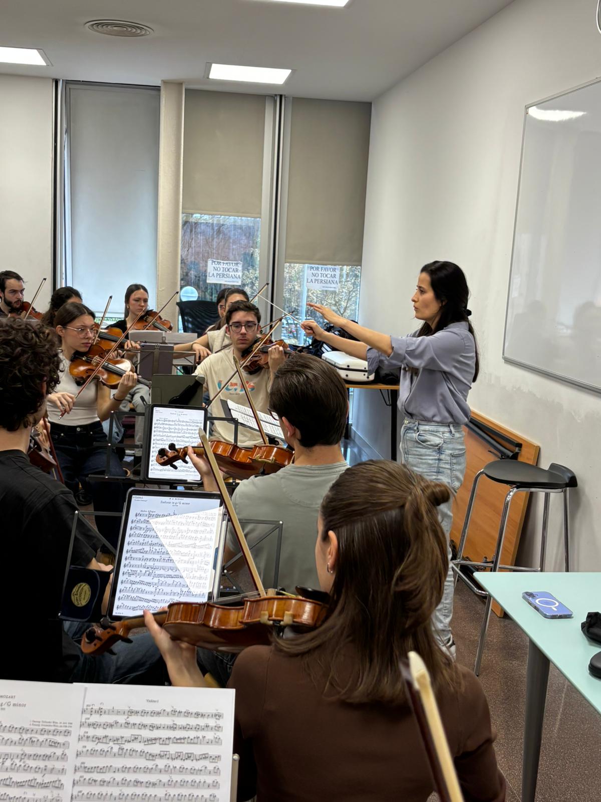 Music class with students playing violins and a conductor leading the group in a classroom.