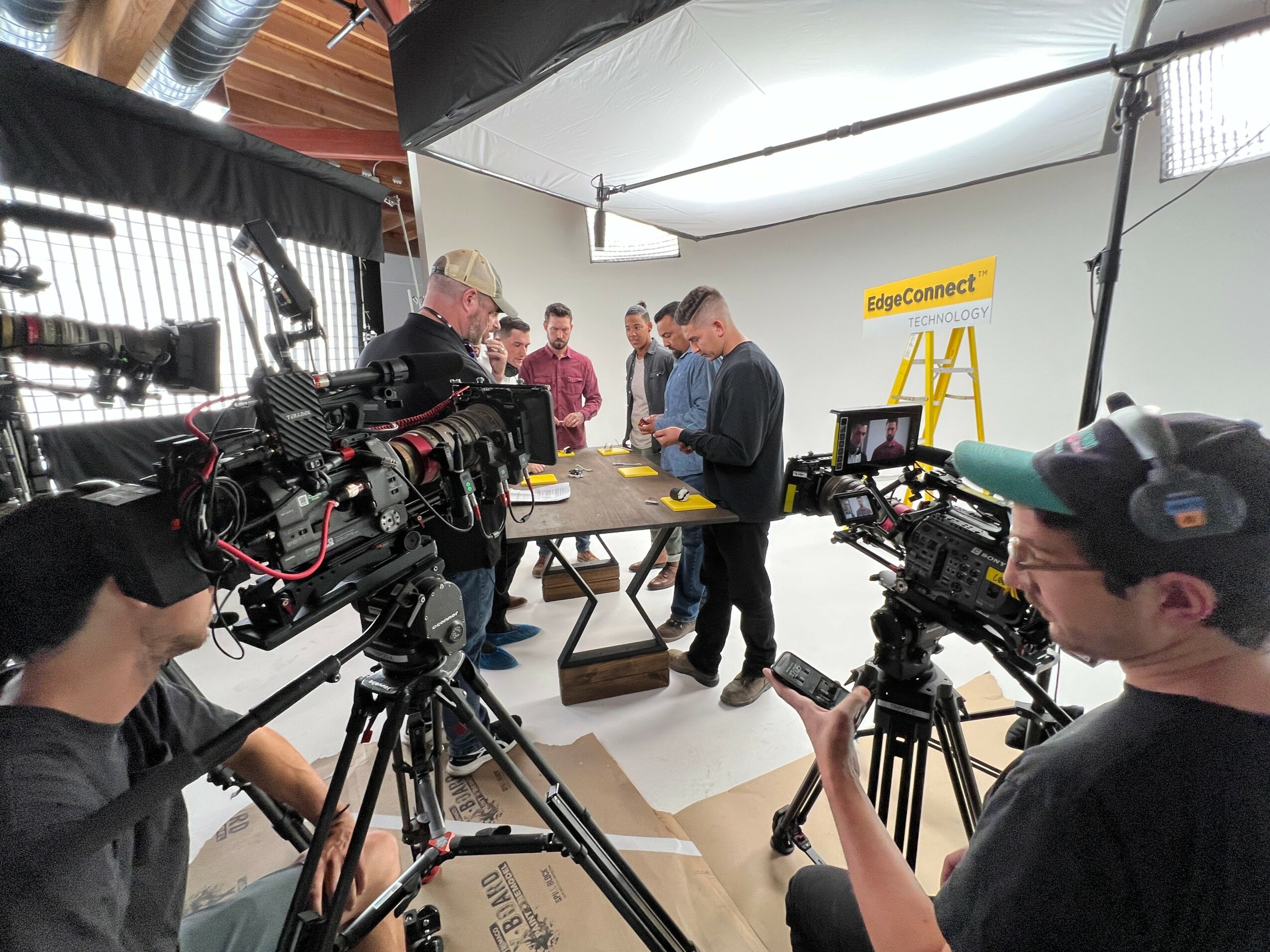 Group of people in a studio with cameras, lighting, and a yellow sign reading 'JoyeConnect' in the background.