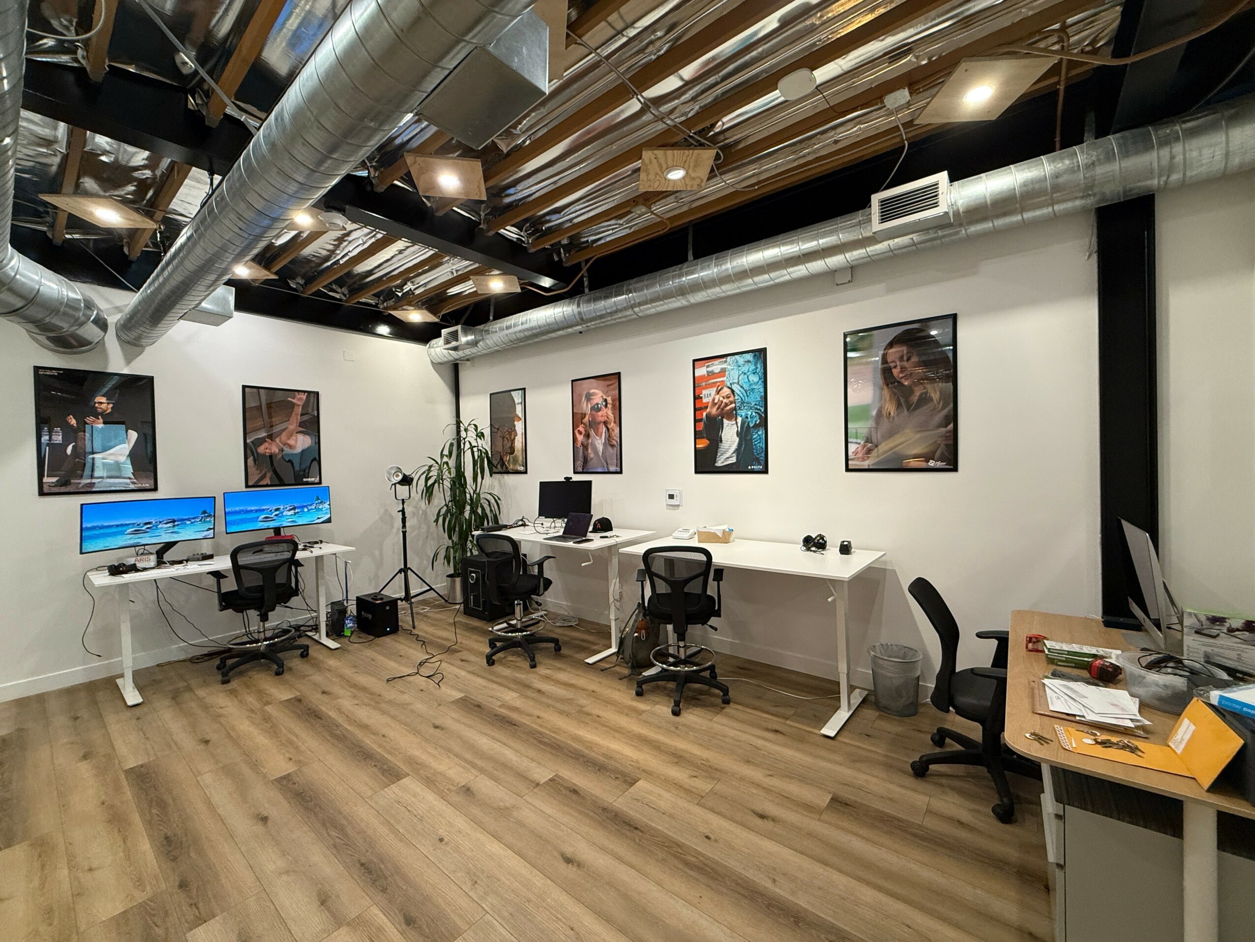 Gallery room with framed photos on white walls, desks with computers, chairs, and a wooden floor.