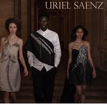 Three models walk down a runway in elegant dresses and suits, with a dark background and wooden interior.
