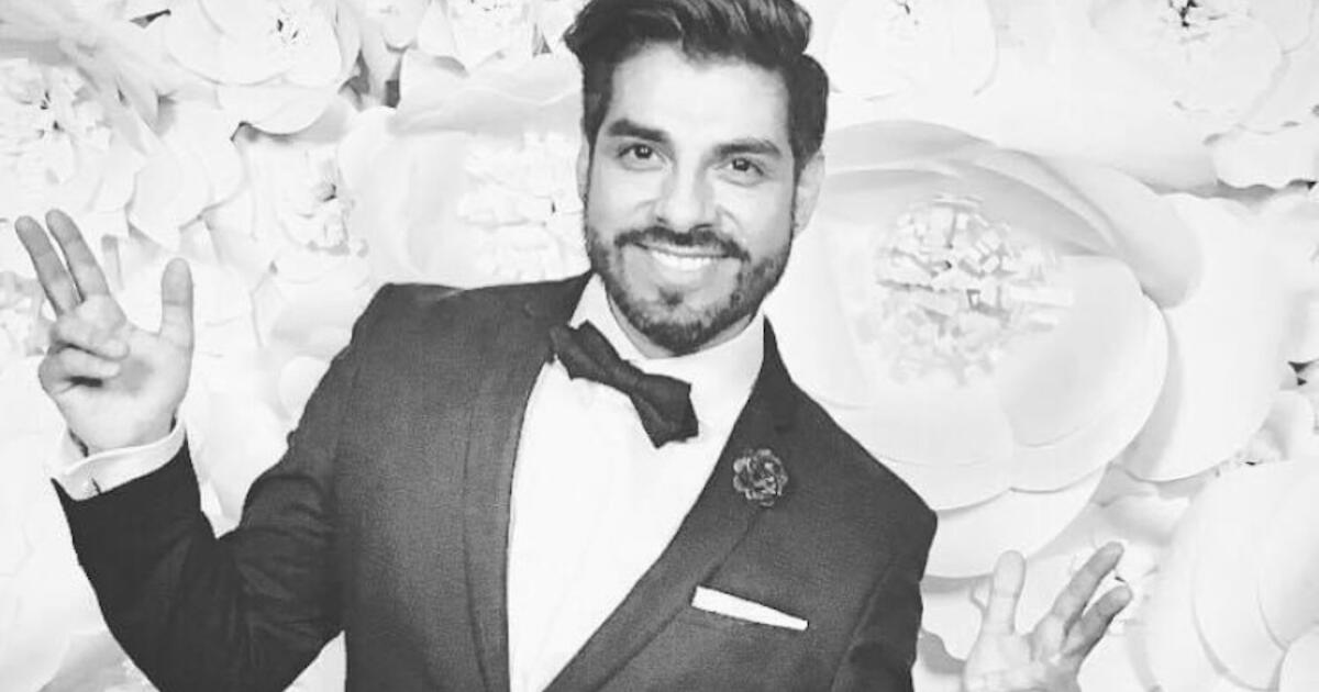 Man in tuxedo smiling and waving, background with floral decorations