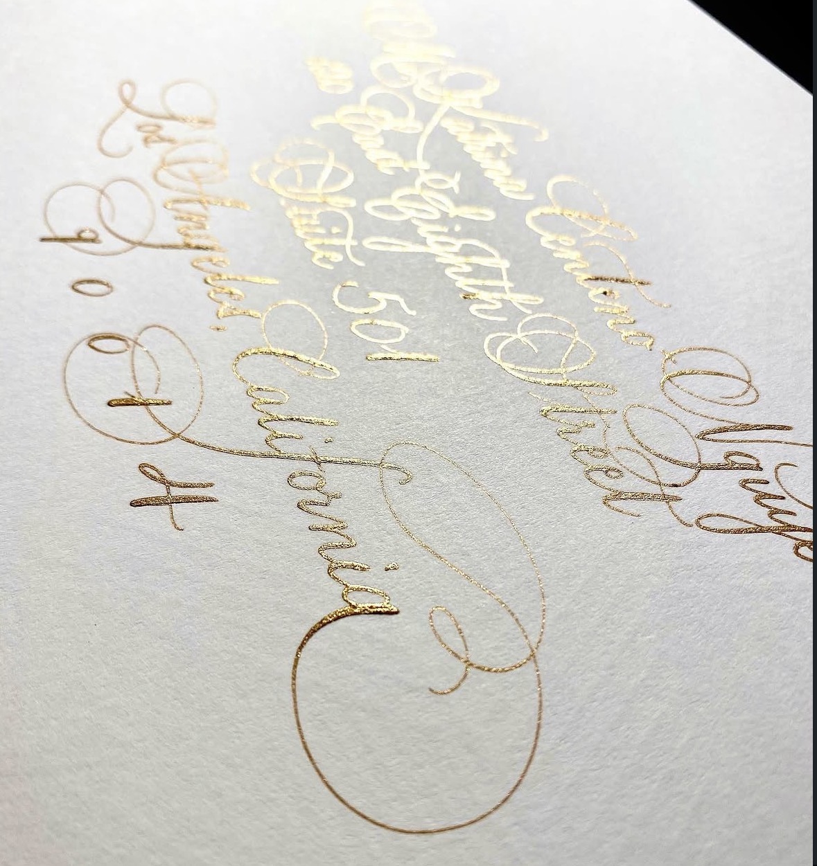 Close-up of elegant gold calligraphy on white paper, angled view, with a black background corner.