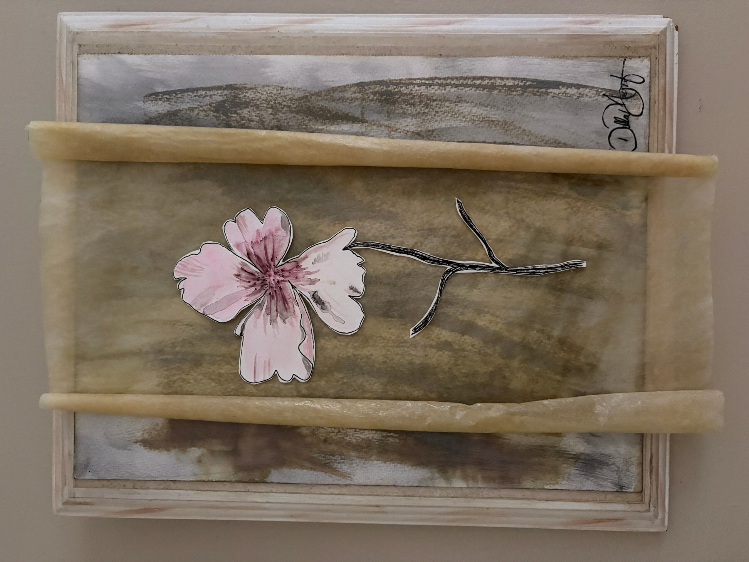 Decorative wooden tray with a pink flower and a small branch, two horizontal wooden sticks across the tray, neutral background.