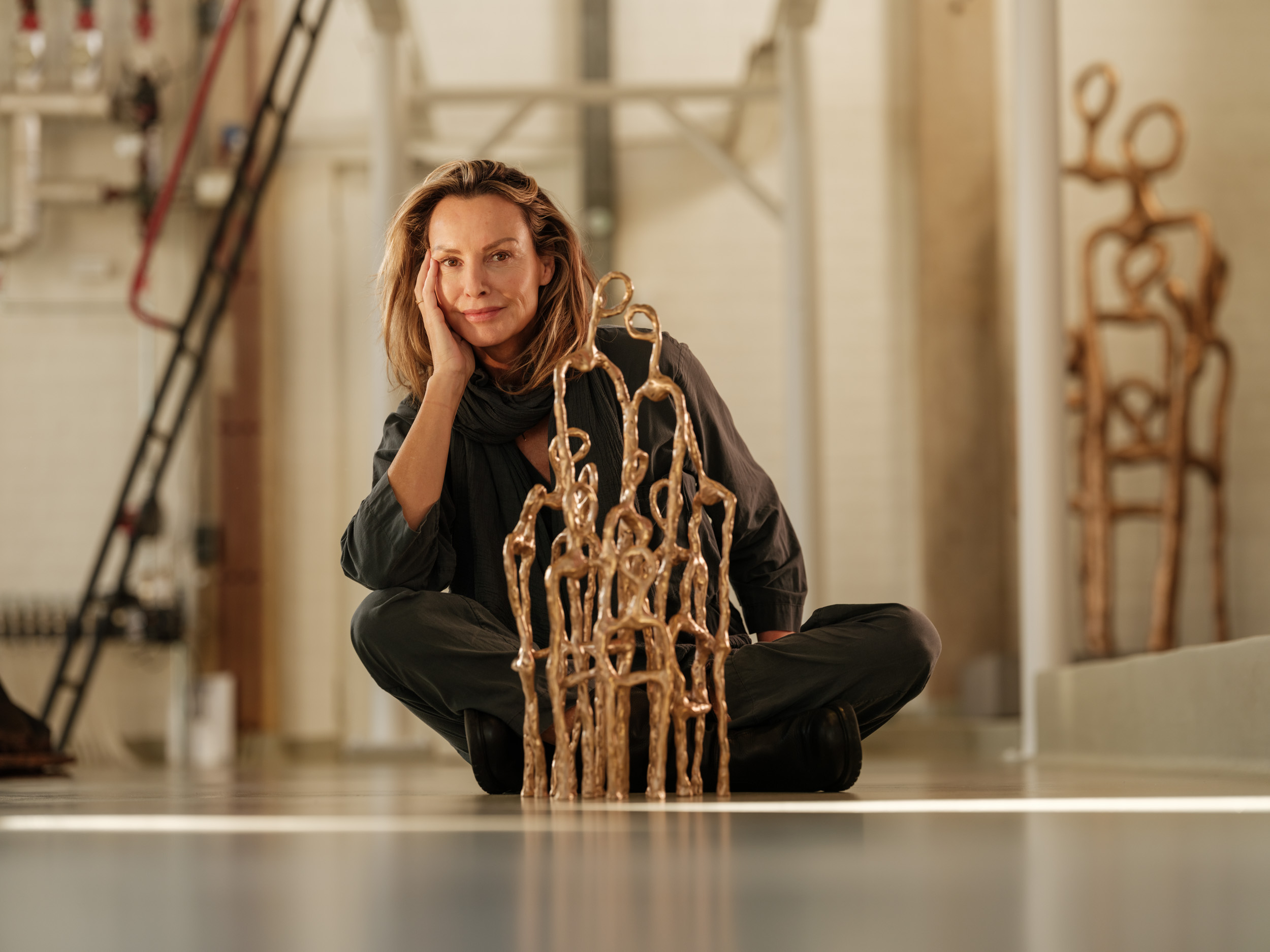 Woman sitting cross-legged on the floor, smiling, with sculptures behind her in an art studio.