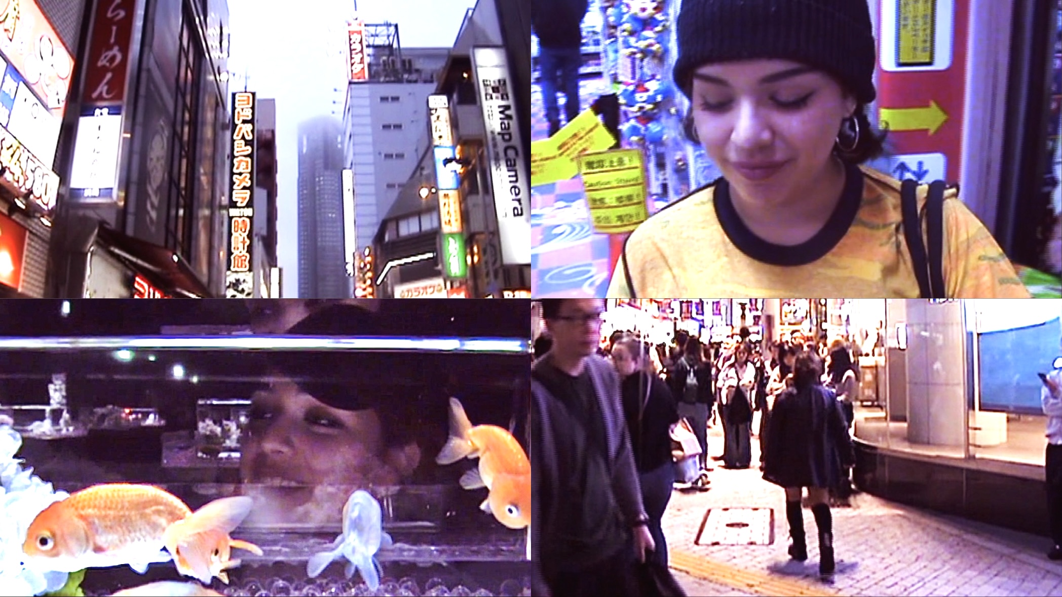 A young woman in a yellow shirt and black beanie smiling, city street with people and bright signs, fish tank with goldfish, reflections.
