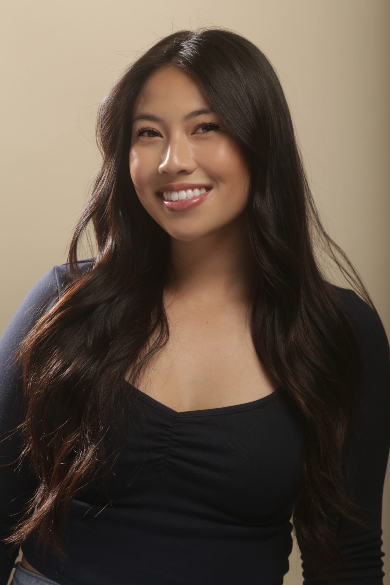Smiling woman with long dark hair wearing a black top and dark blazer, standing against a neutral background.