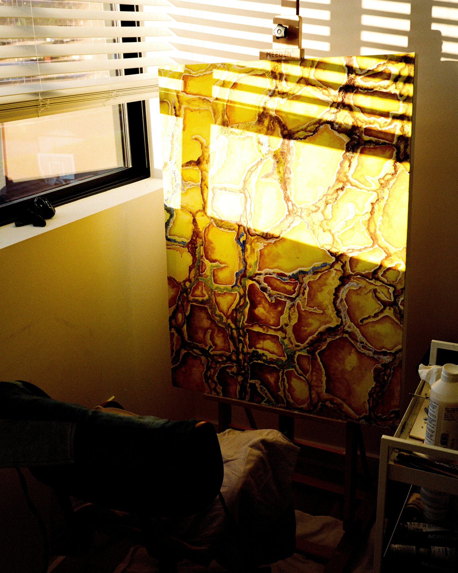 Sunlight through blinds illuminates a marble-patterned lamp on a stand, casting shadows on the wall, with a window nearby.