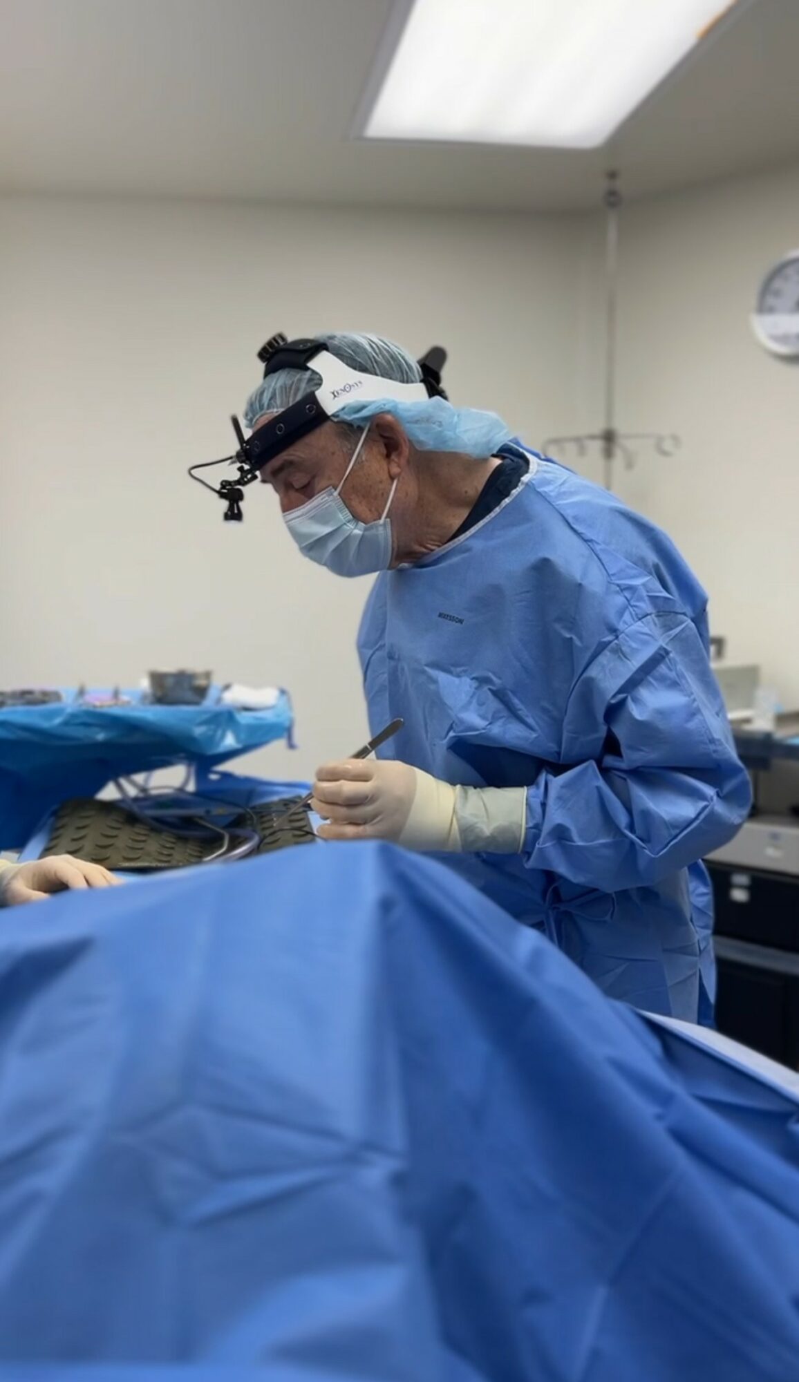 Medical professional in scrubs, mask, and gloves performs a procedure in an operating room.