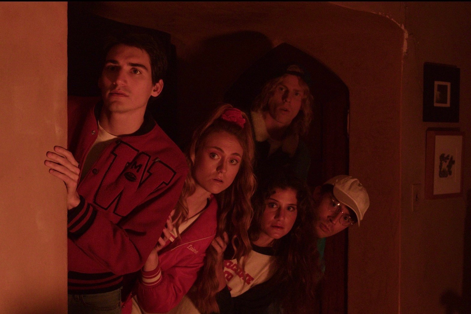 Four people standing in a dimly lit room, looking to the side with serious expressions.